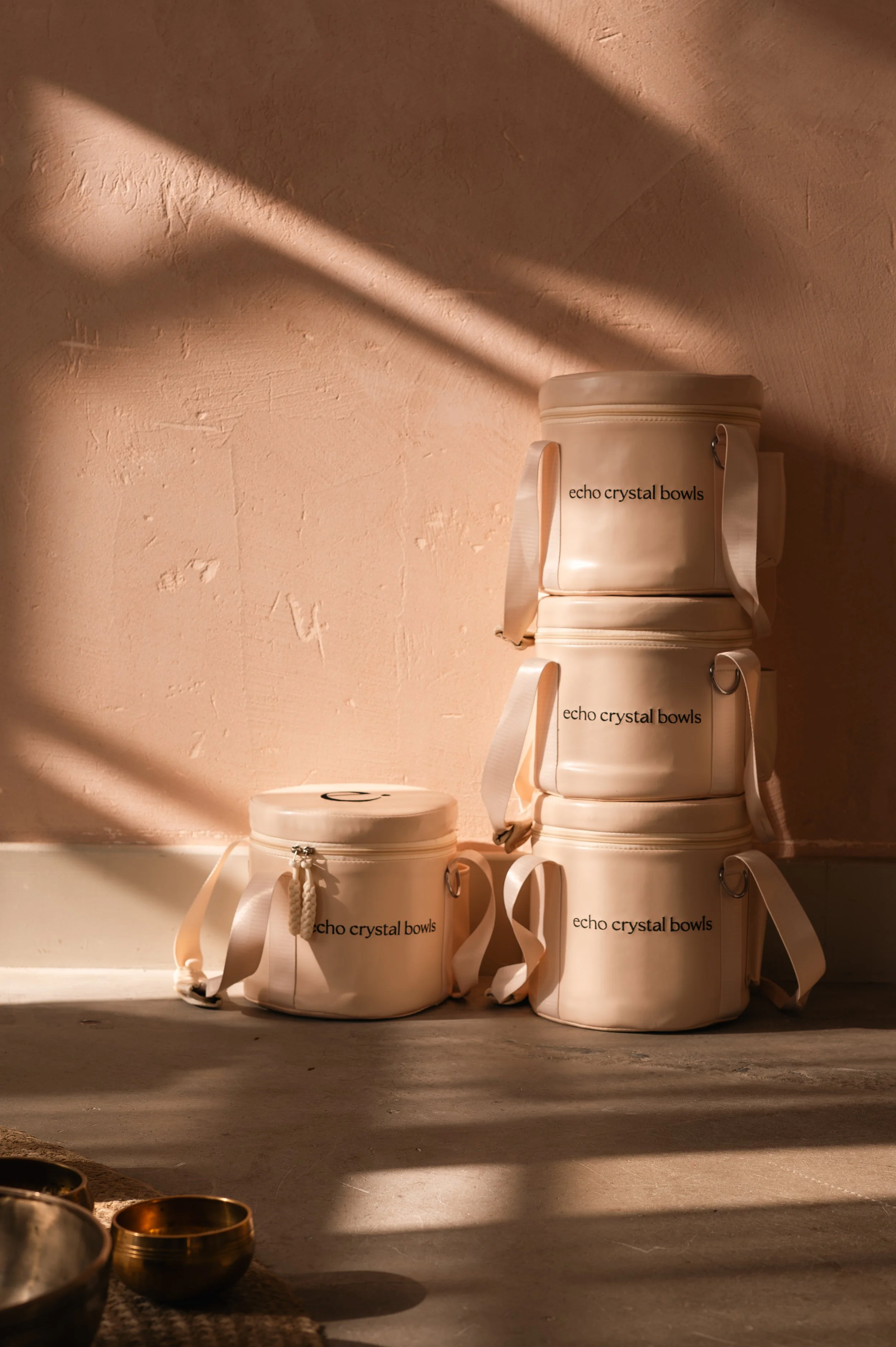 Stacked white cylindrical echo crystal bowls with lids, sitting against a pink textured wall with sunlight casting shadows.