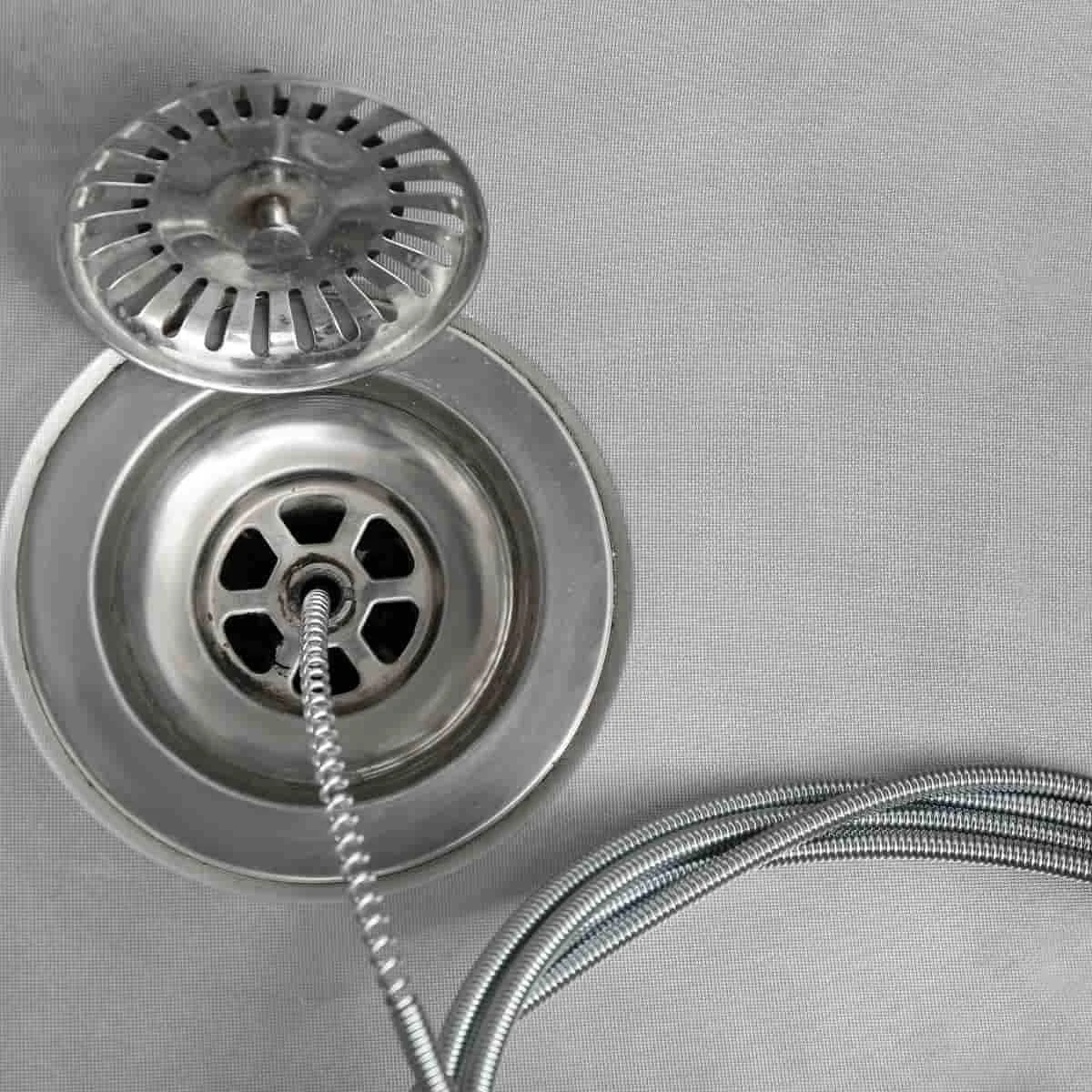 a drain snake going down the drain of a stainless steel sink