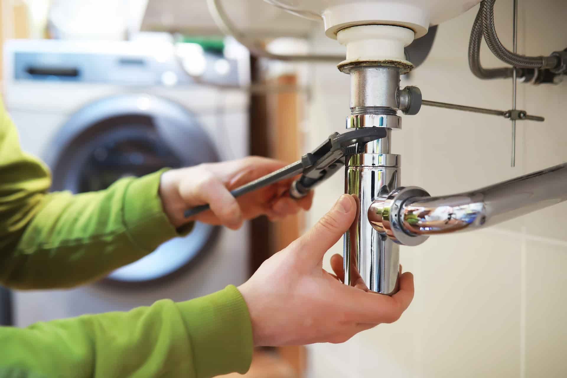 a man tightening plumbing pipes under a sink