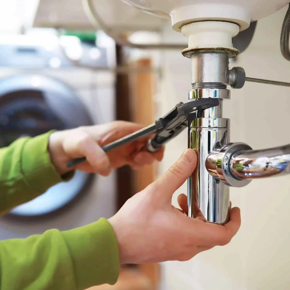 two hands tightening a a pip with a wrench in a bathroom