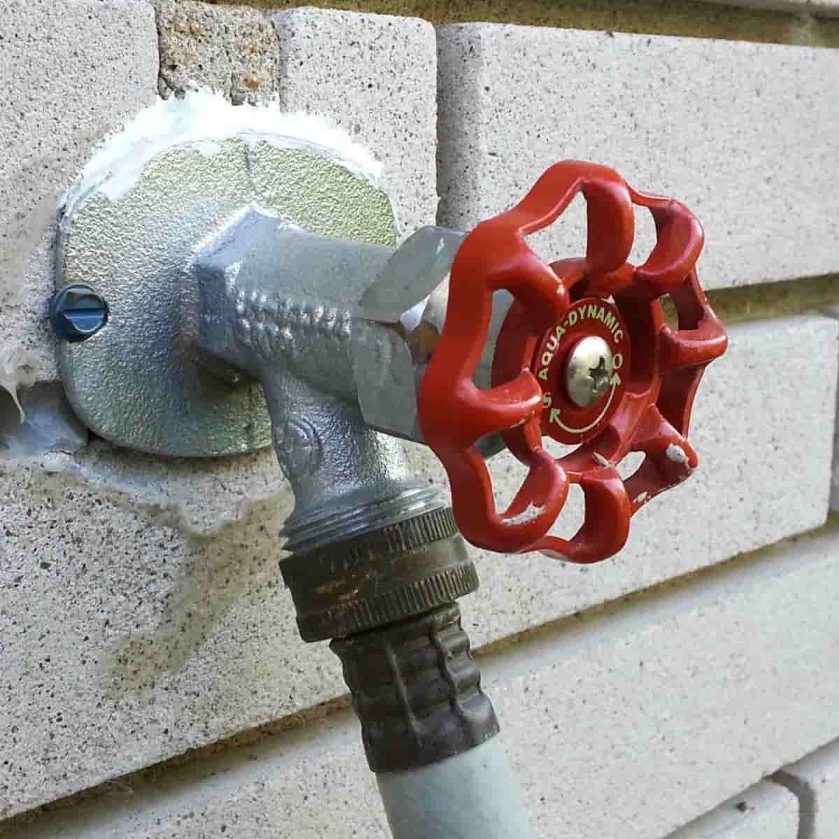 an outdoor hose bib with red handle on the side of a home