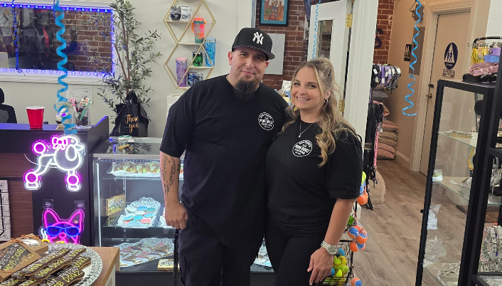 A man and woman standing inside a store, smiling at the camera, with colorful decorations and display cases around them.