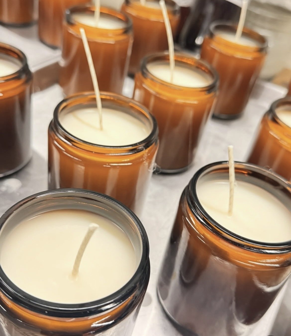 Multiple amber glass jars filled with white candle wax and wicks ready for candle making.