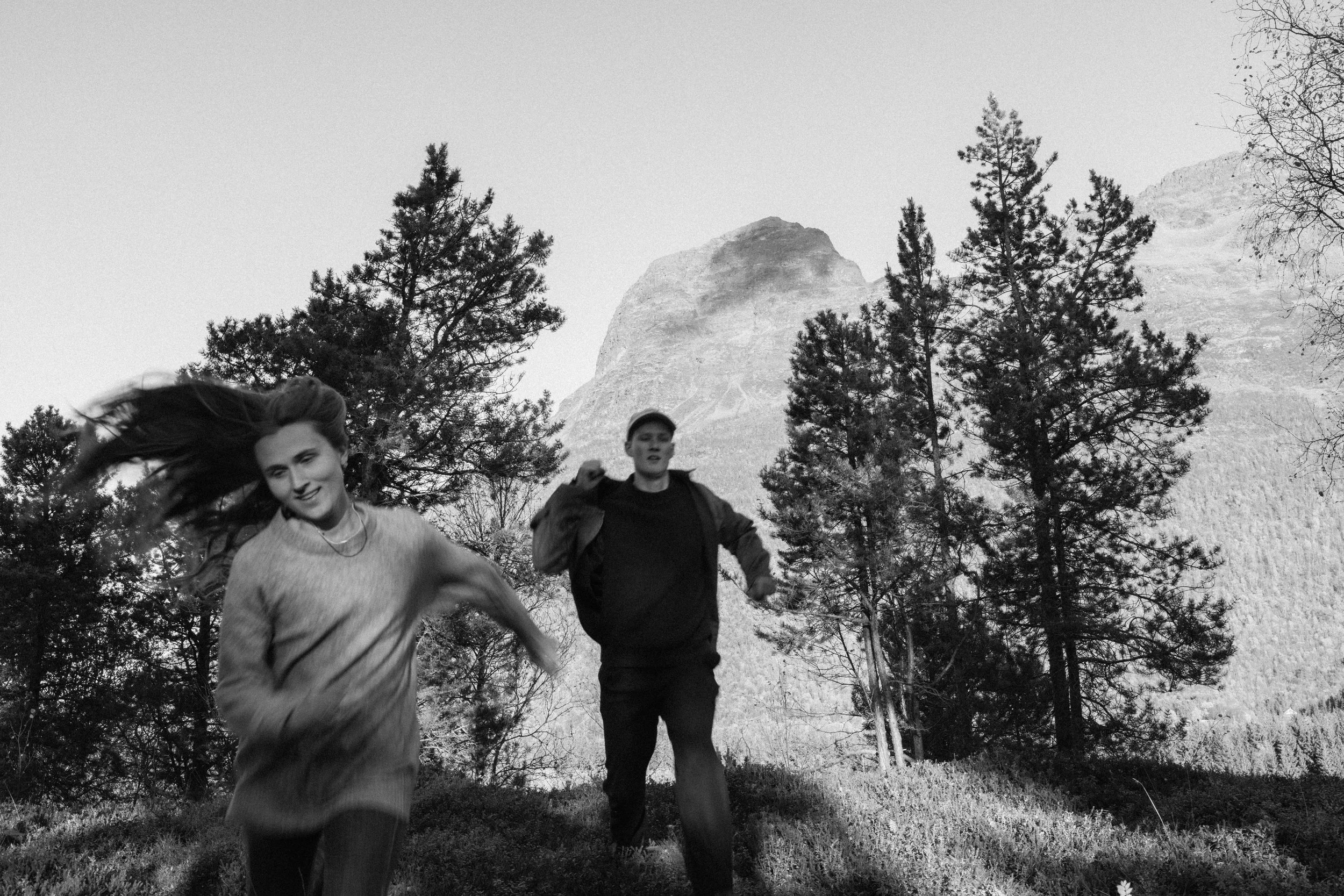 Two people running outdoors in a forested area with mountains in the background.