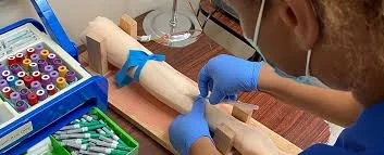 A phlebotomy student training on a skills trainer