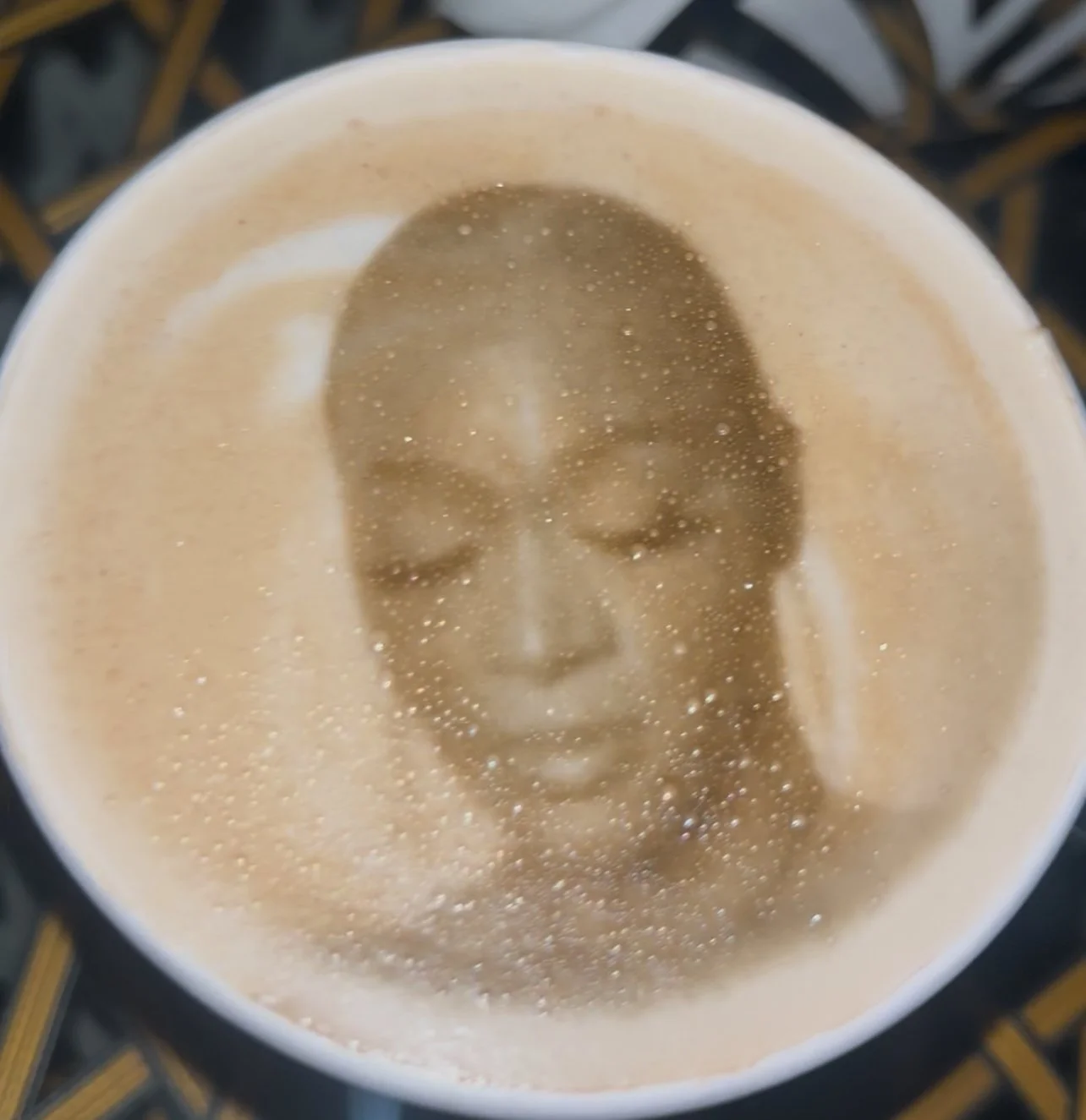 A coffee cup with a printed face of a woman wearing glasses, with steam and bubbles on the surface.