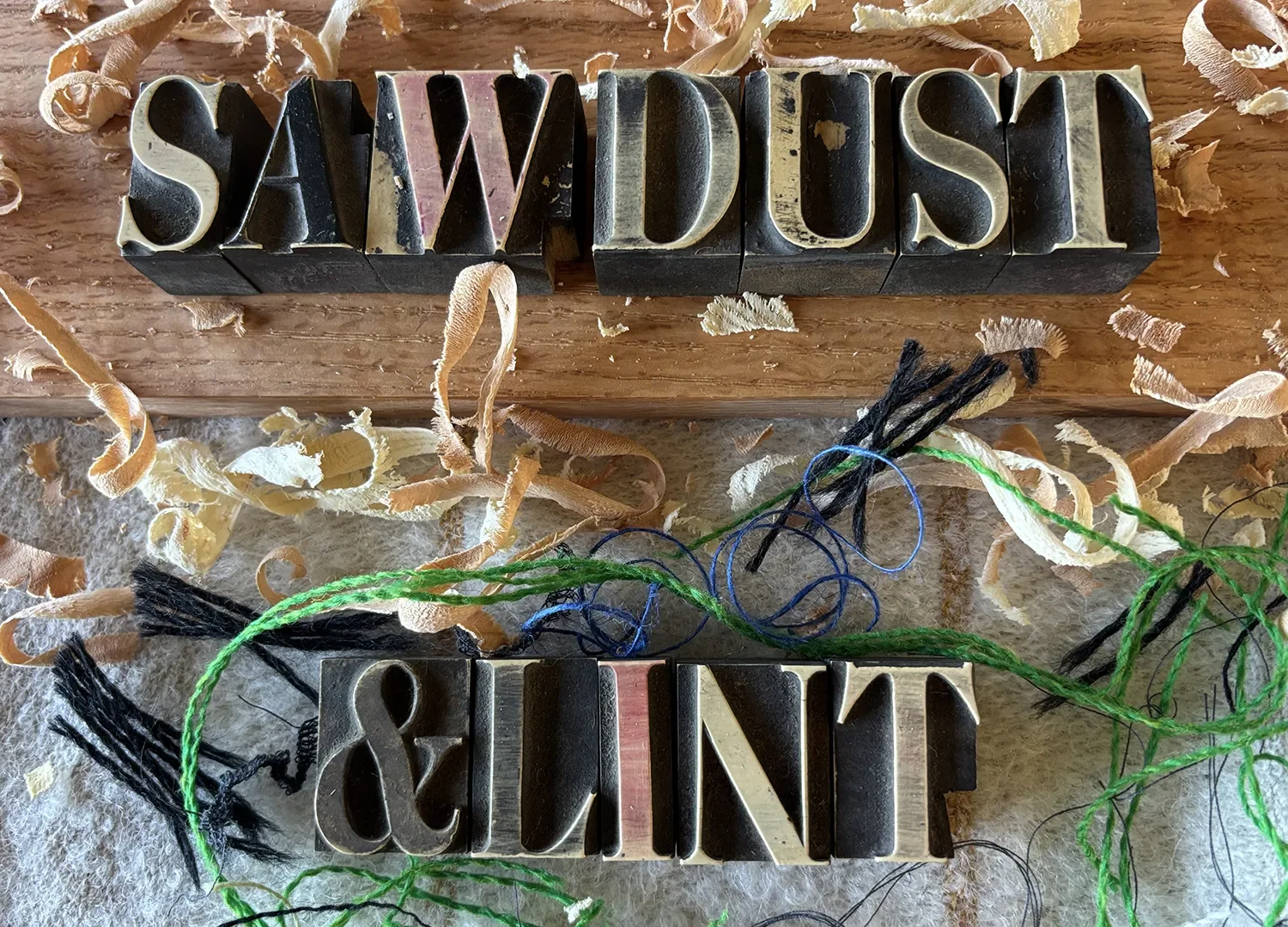 Sawdust & Lint in type letters on a table with wood shavings and textile scraps