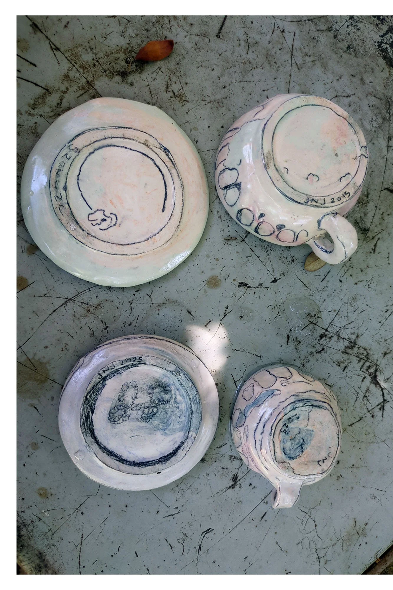 Bottoms of all four porcelain pieces showing artist signature JNJ 2025