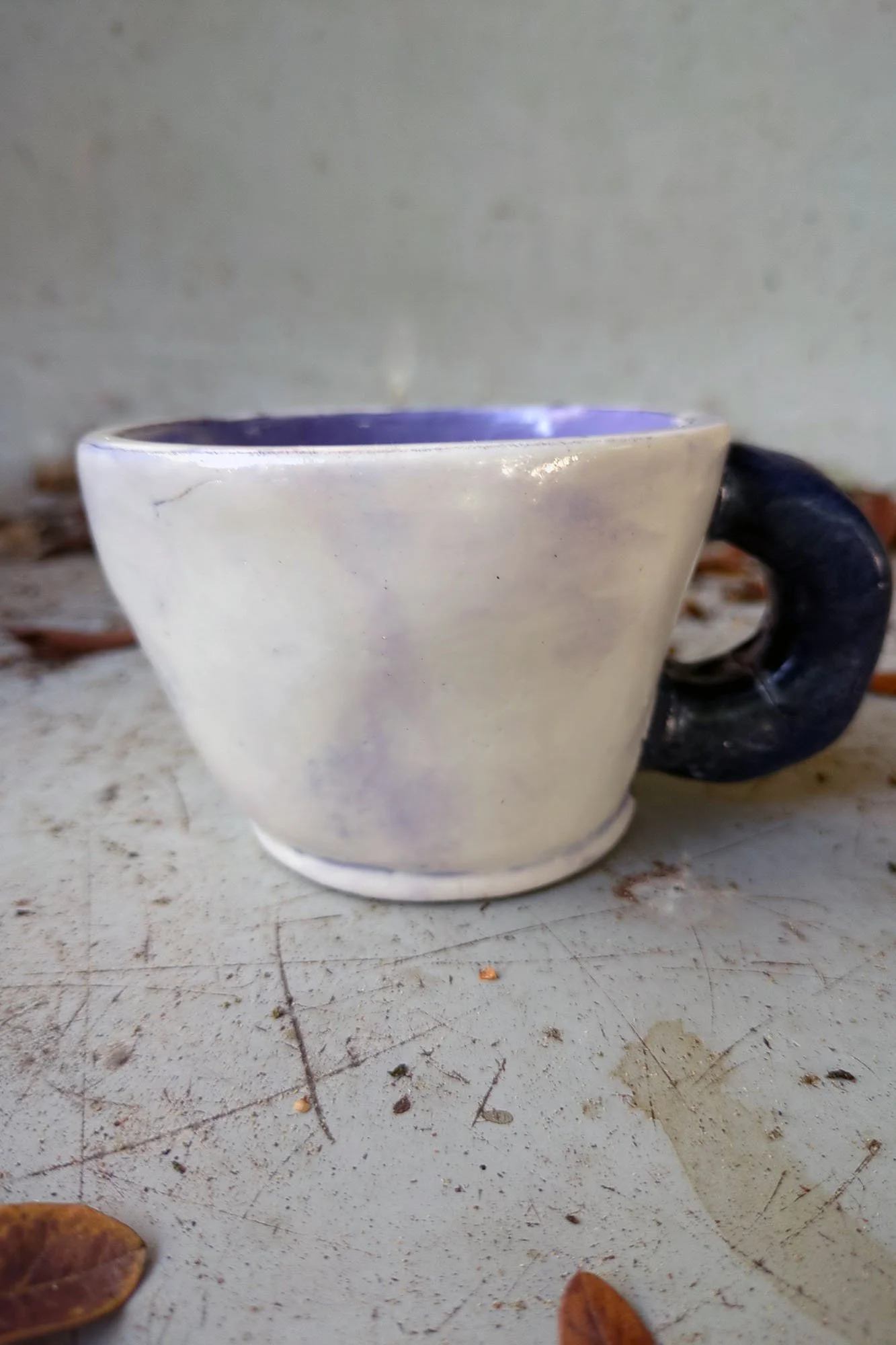 Back view of handmade porcelain cup, white glaze with soft lavender blush and sculptural black handle