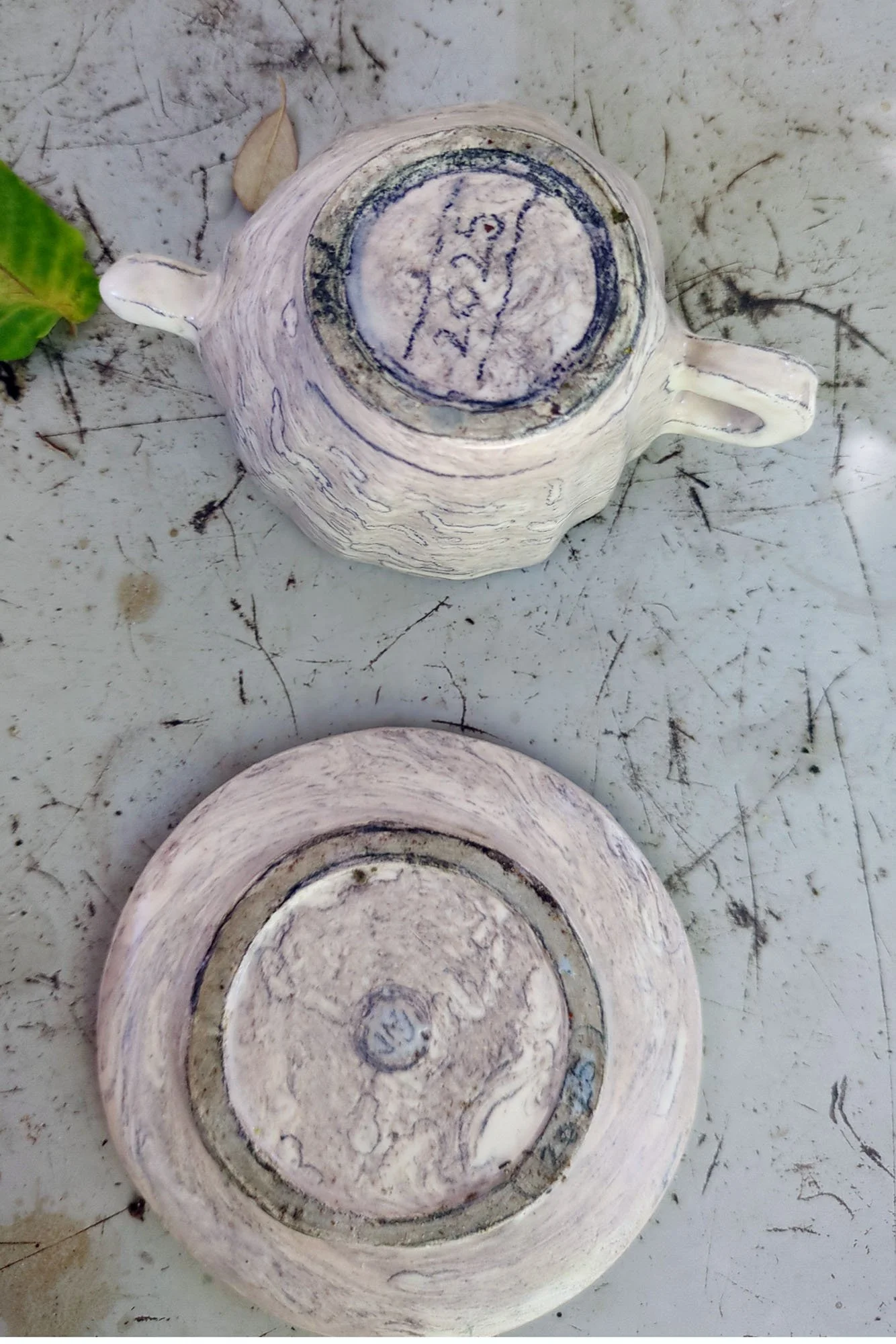 Bottoms of handmade marbled porcelain cup and saucer showing artist signature JNJ 2025