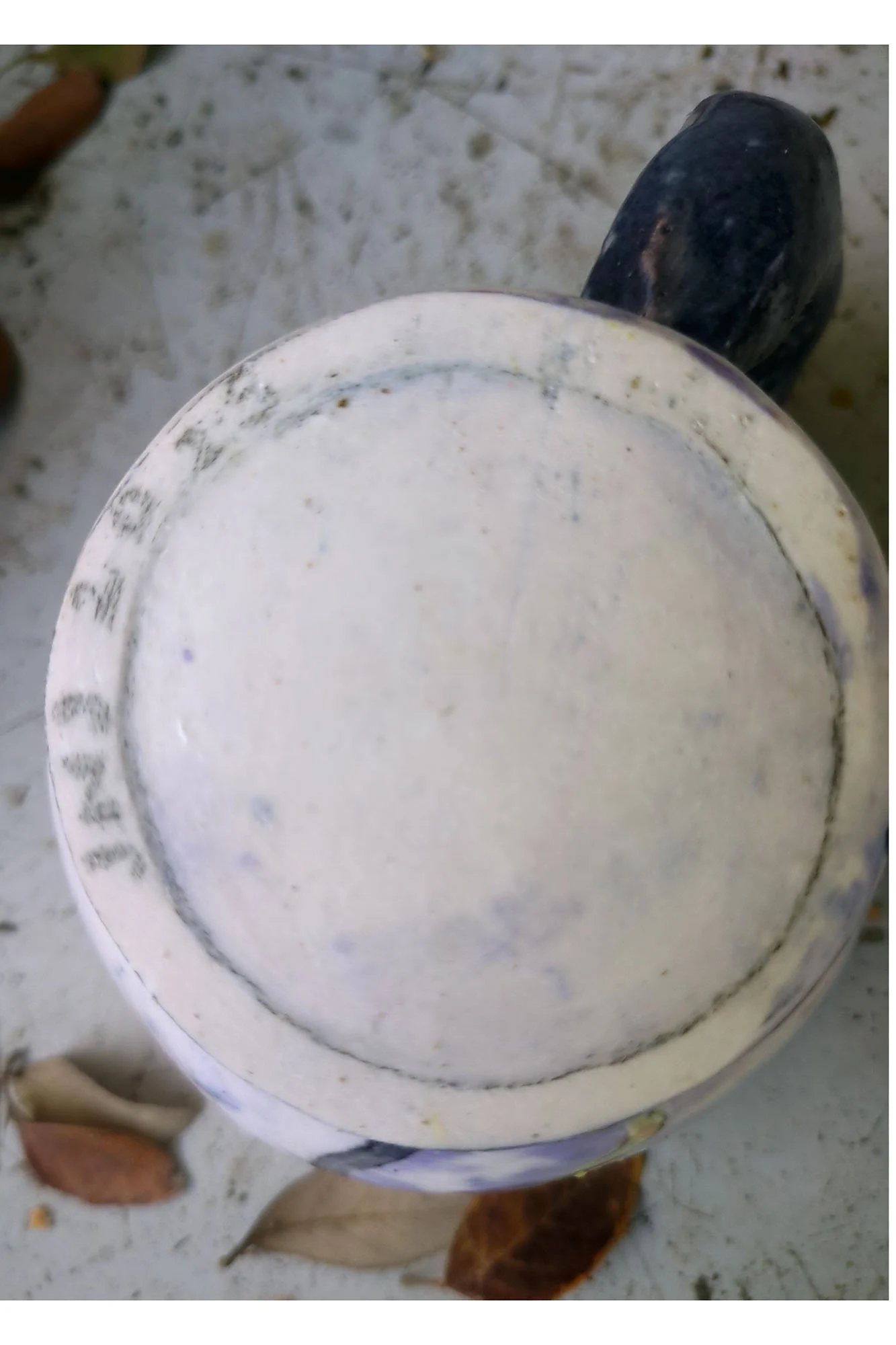 Bottom of hand-built porcelain cat cup showing unglazed foot ring and artist signature and date