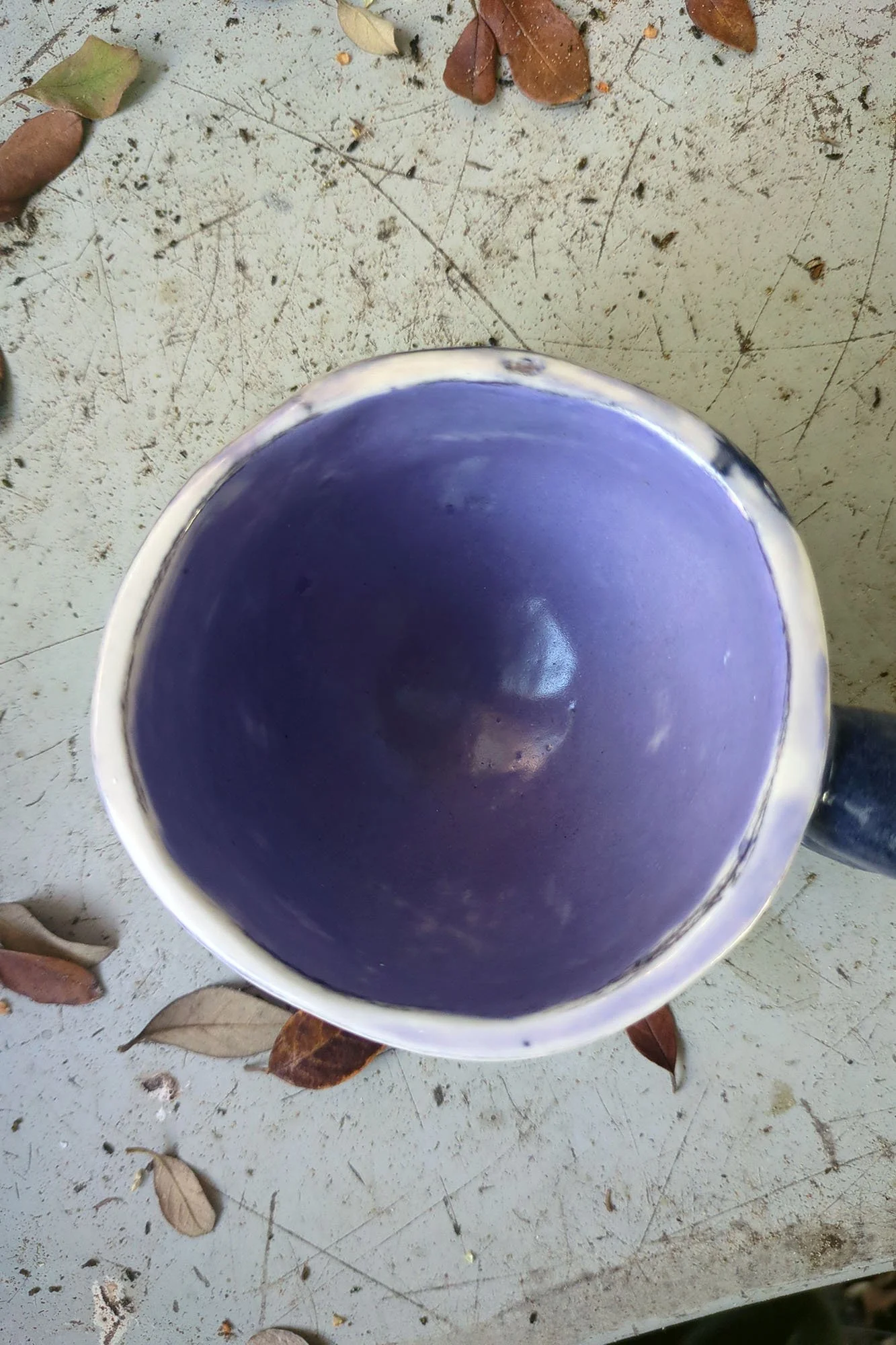 Overhead view into deep lavender interior of handmade porcelain cup with black handle