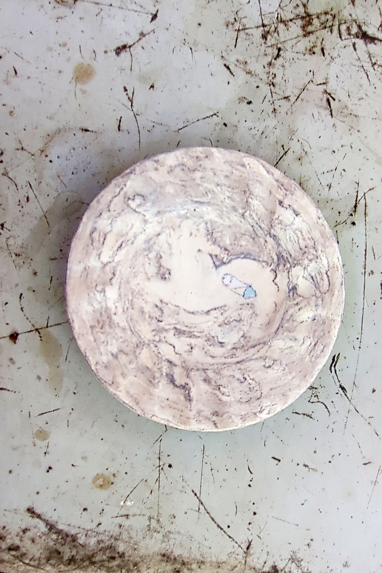 Overhead view of handmade porcelain saucer alone, marbled brown and white glaze with small blue and white drawing near the center