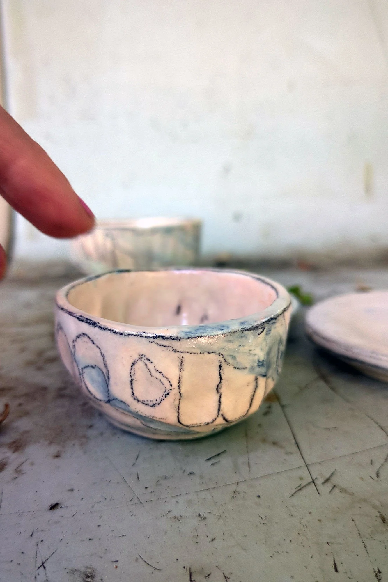 Small handmade porcelain cup with finger for scale, showing glaze depth and texture