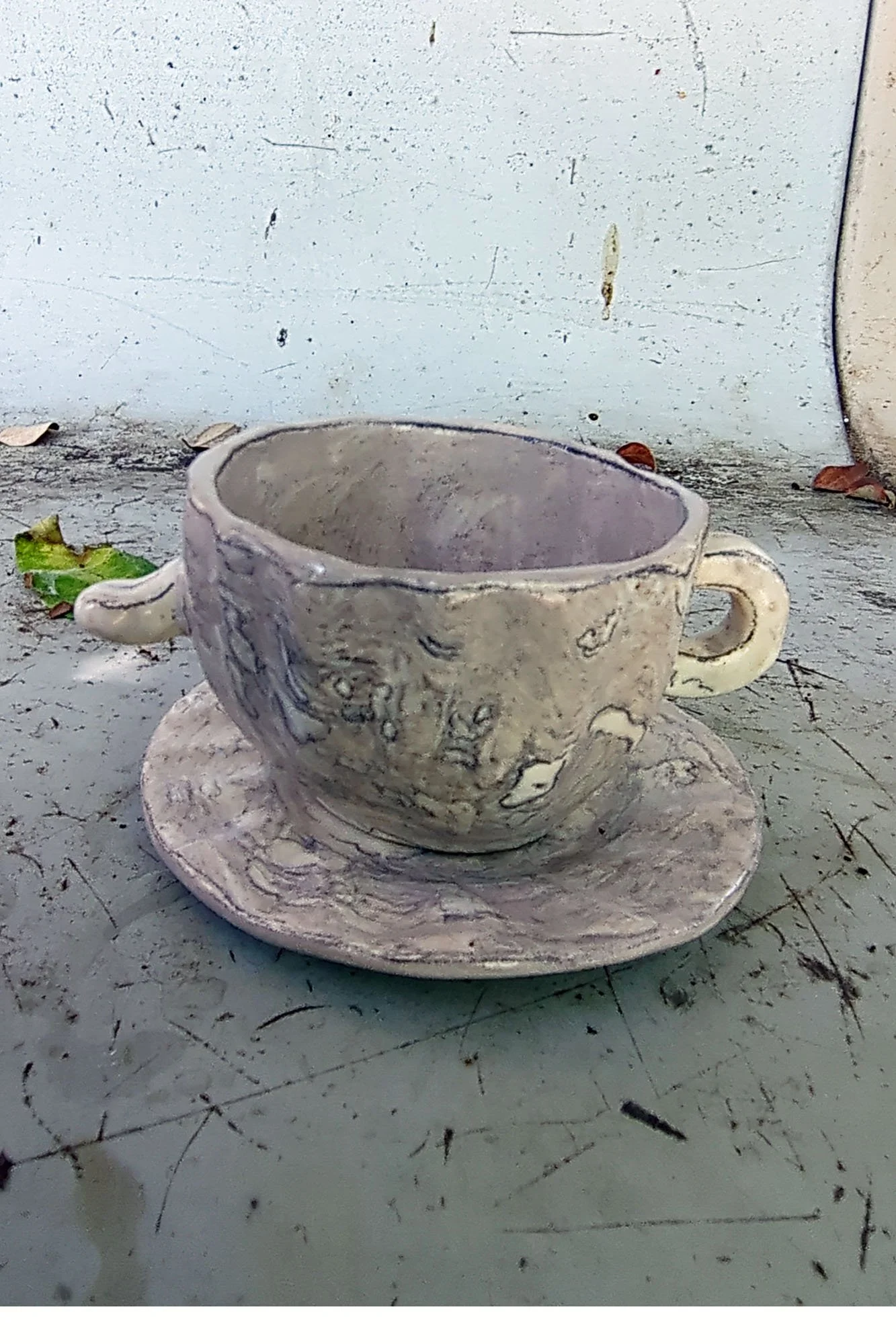 Right side view of marbled studio porcelain cup on saucer showing rounded form and nub handle detail