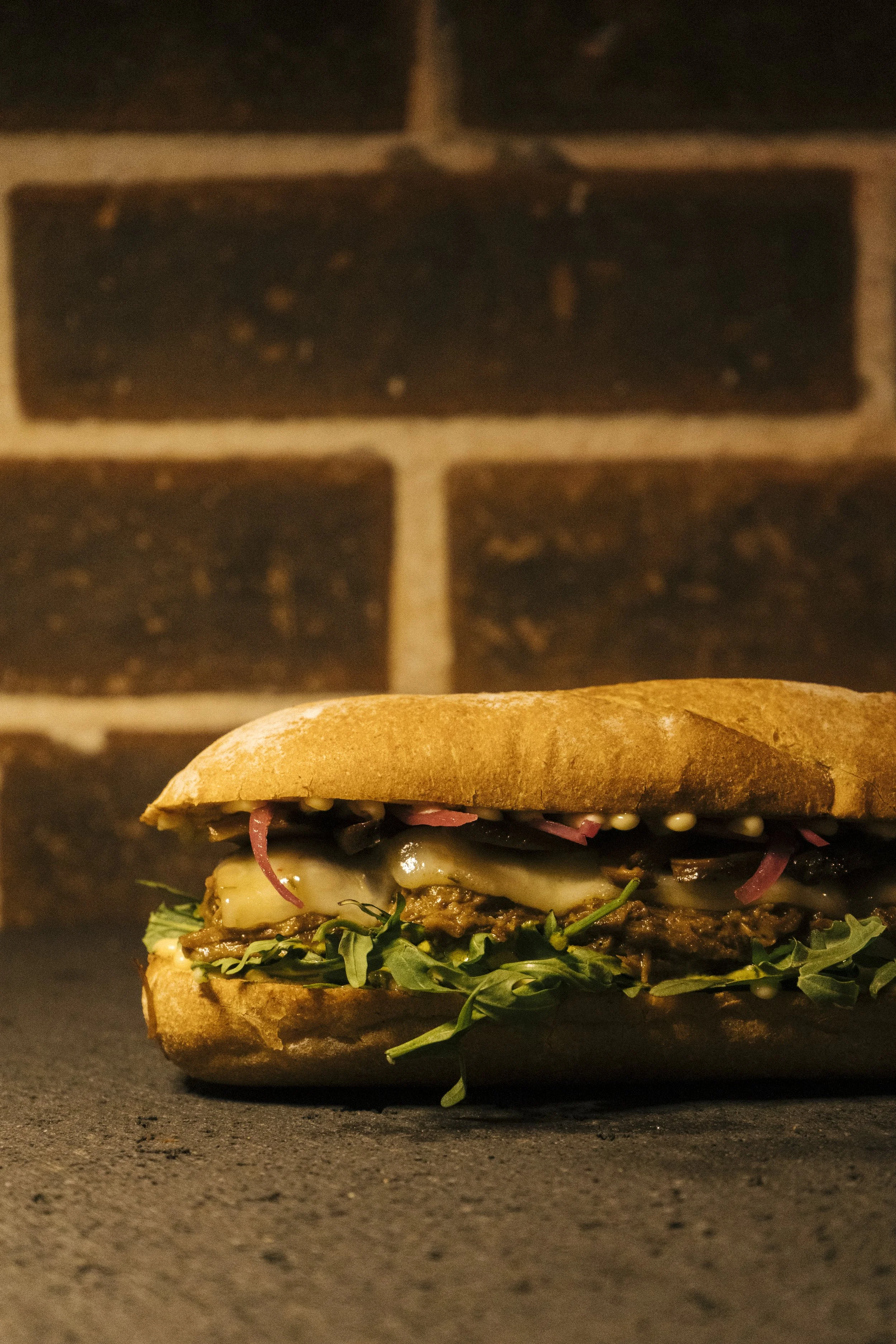 Increíble sándwich Beef Short Rib con costilla de res desmenuzada, queso pepper jack, arúgula, shiitakes encurtidos, salsa de cilantro, mayo de miso y cebollas encurtidas en pan baguette de Comma - Sandwich Social Club, zona 14 Ciudad de Guatemala.