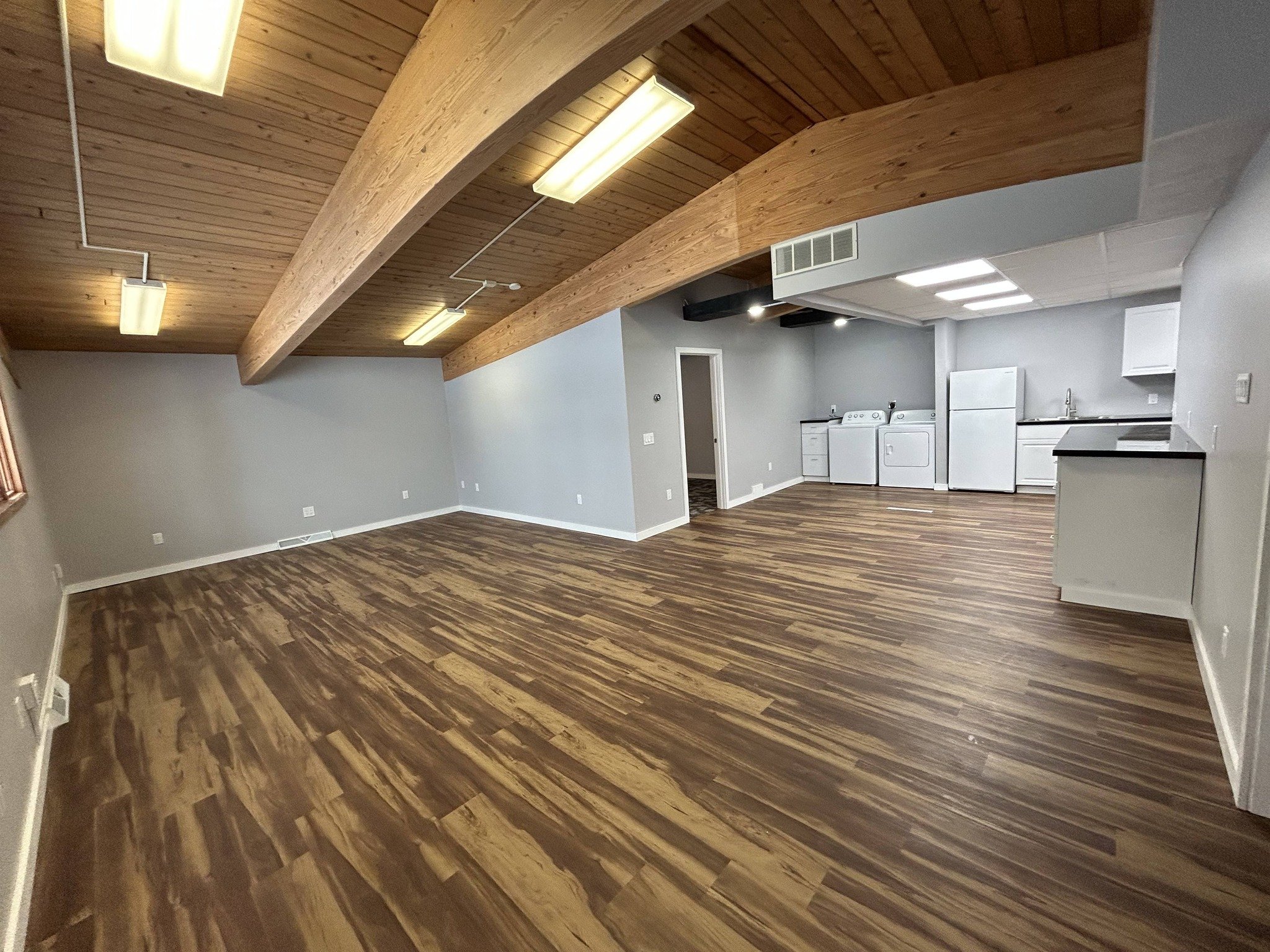 Open living or dining room with wood-paneled ceiling, fluorescent lighting, hardwood floors, and a laundry area with washing machine and dryer.