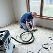 A person vacuuming a carpet in a room with a window and sunlight.