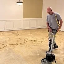 Man operating a floor polishing machine in a room with beige walls and white wainscoting.