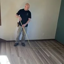 Man installing or adjusting hardwood flooring in a room with green walls.