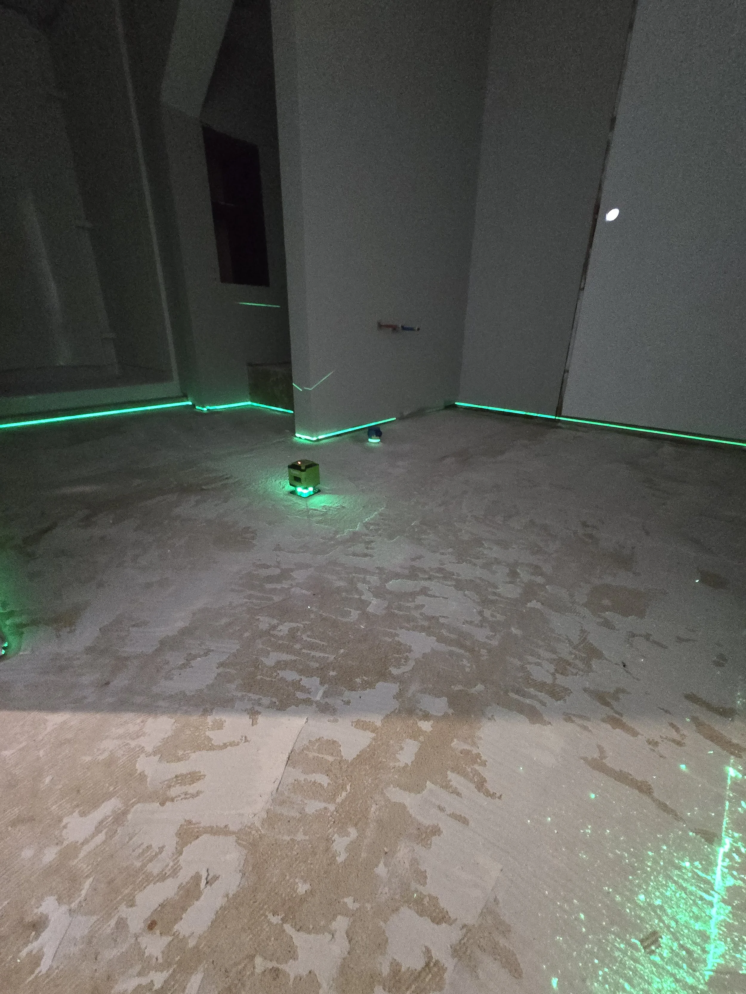 A dark room with green laser lights along the floor and wall, and some electrical wires and a small green object on the floor.