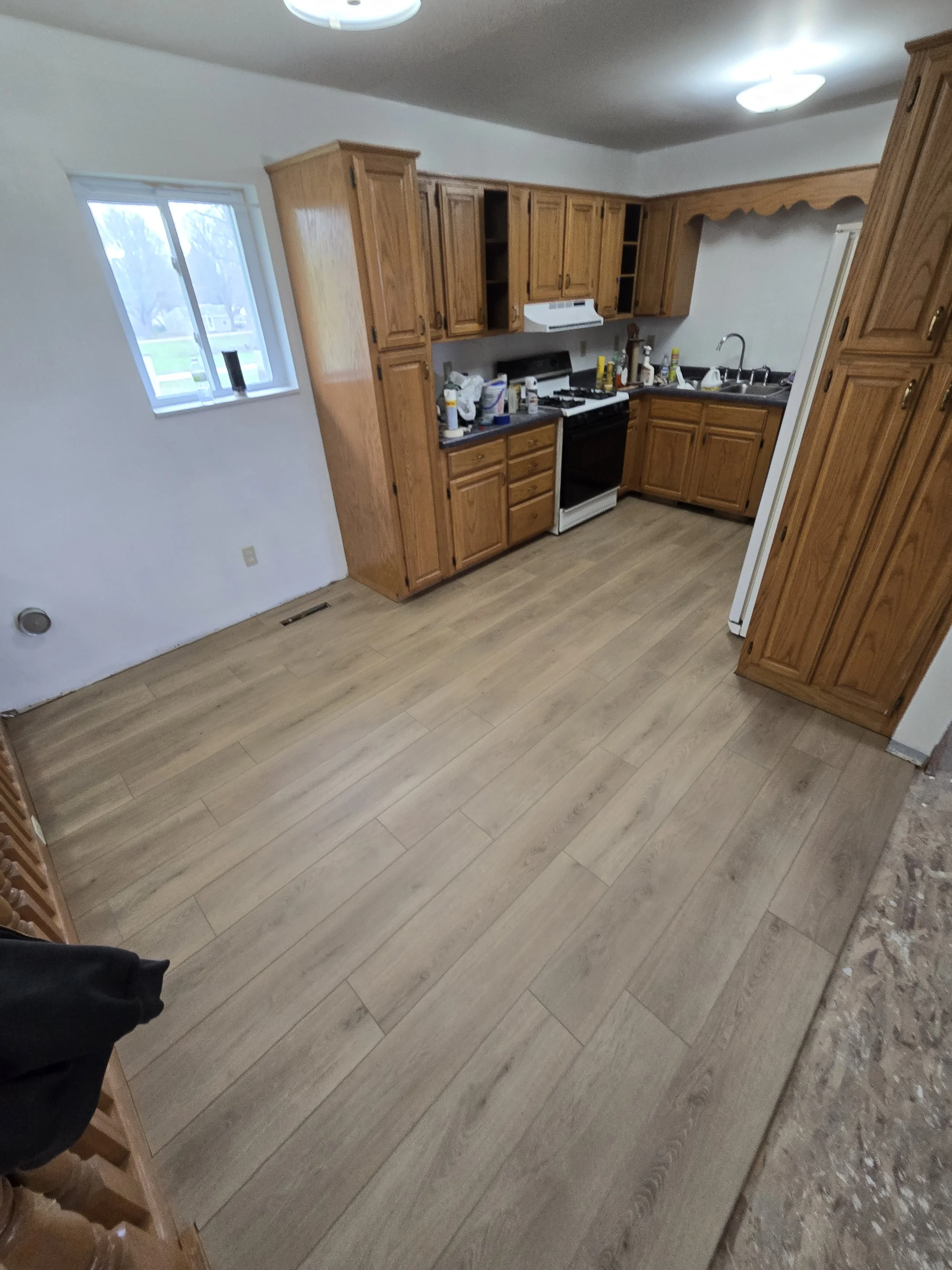 Kitchen with wooden cabinets, a window, a stove, a sink, and various kitchen items on the countertop, and light-colored wood flooring.