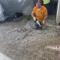 Worker in orange shirt using a power tool to cut or grind a brick or stone surface.