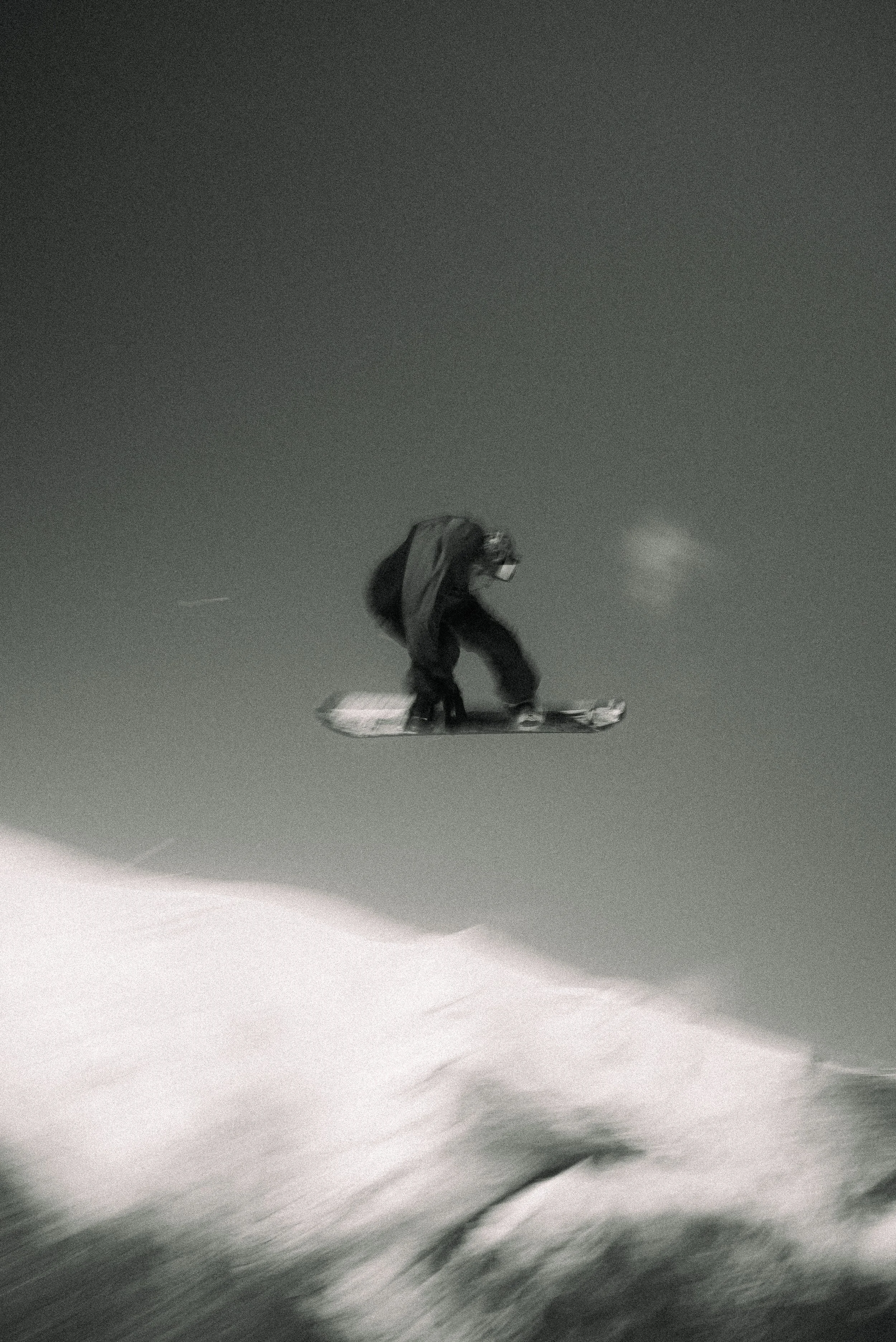Nighttime scene of a person snowboarding down a snow-covered slope, dressed in dark winter clothing and a backpack, against a dark sky.