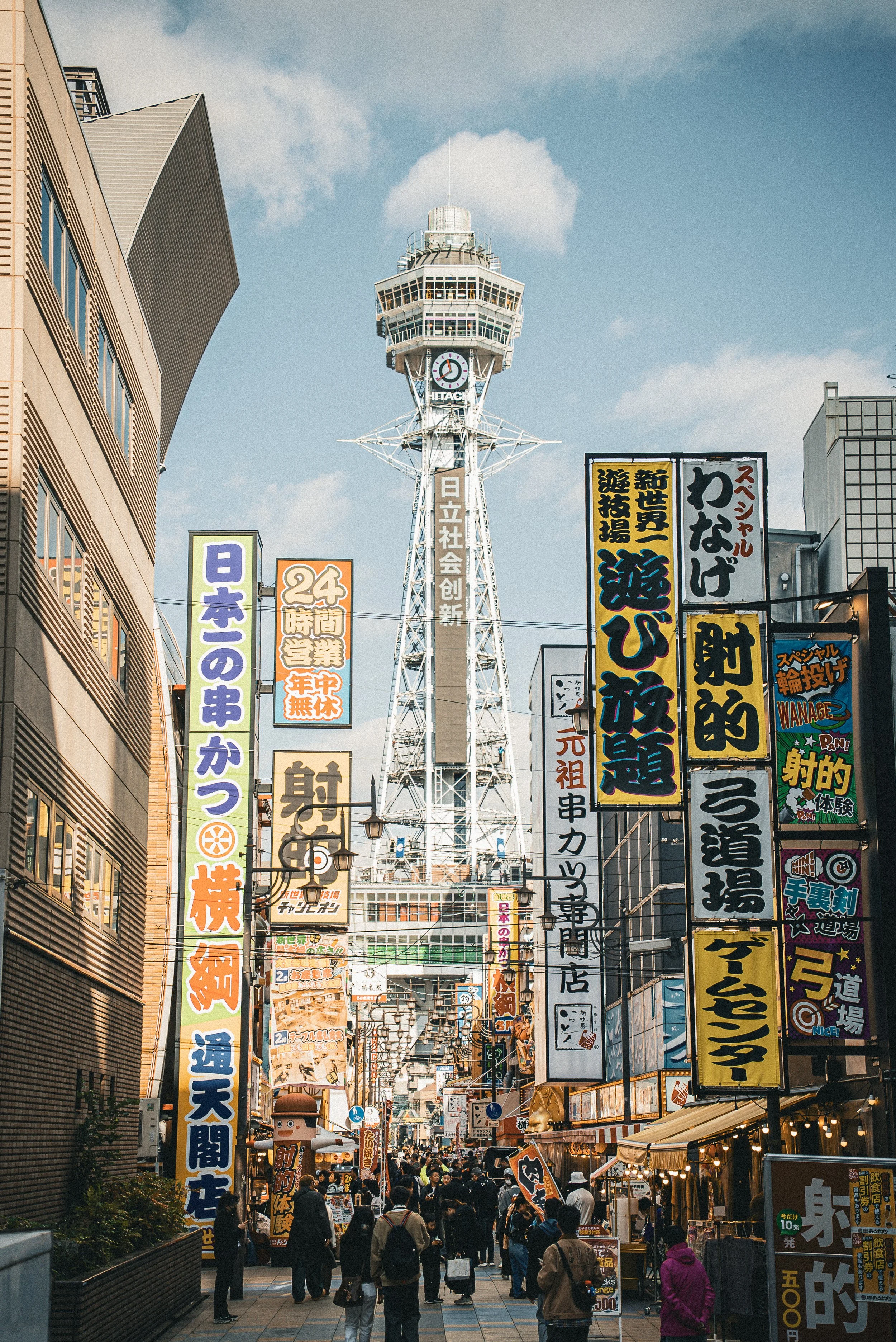 Busy street in Tokyo with numerous colorful signs in Japanese and a tower in the background.