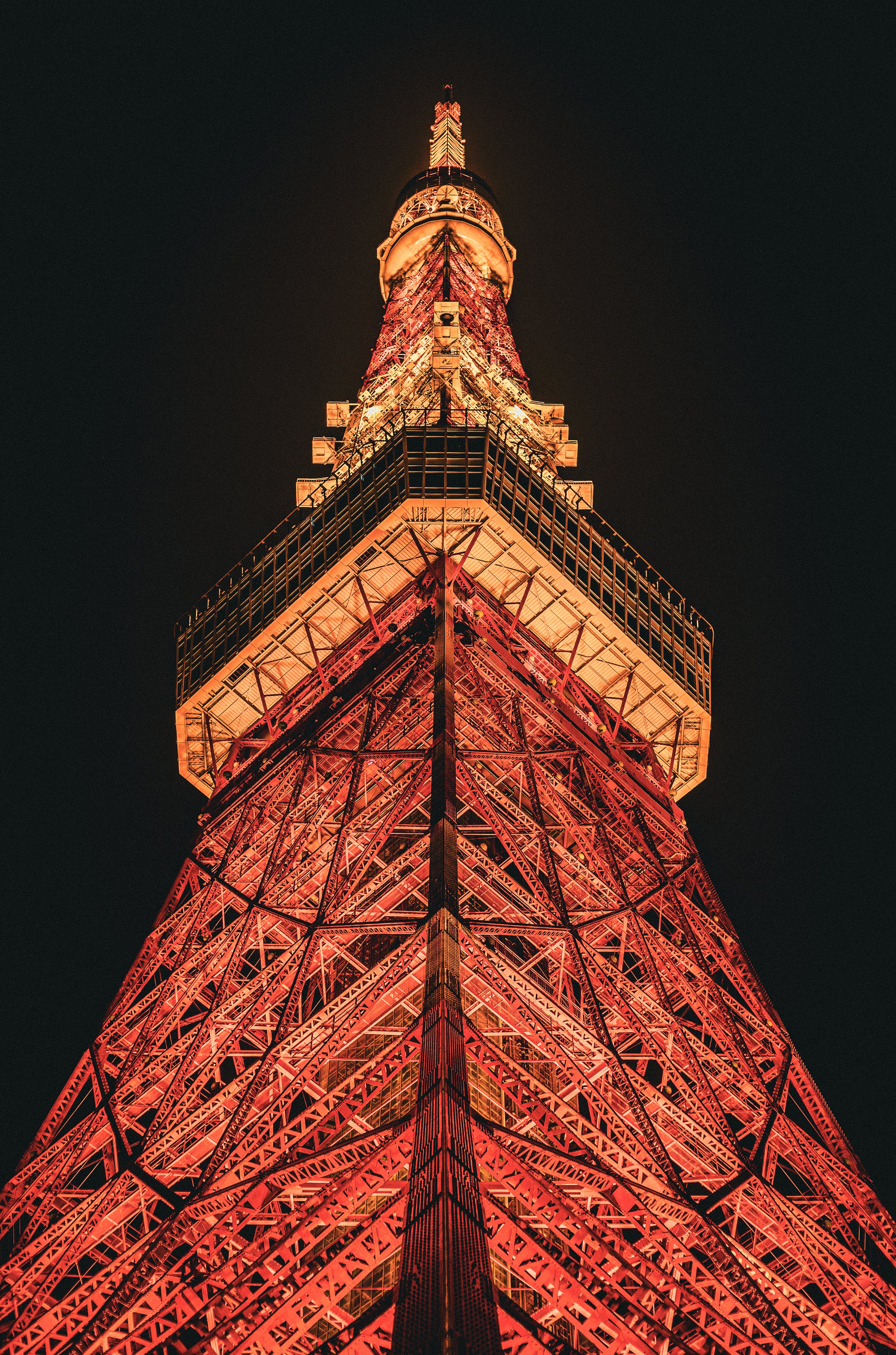 Night view of Tokyo Tower illuminated in orange and red lights, showing its lattice structure against a dark sky.