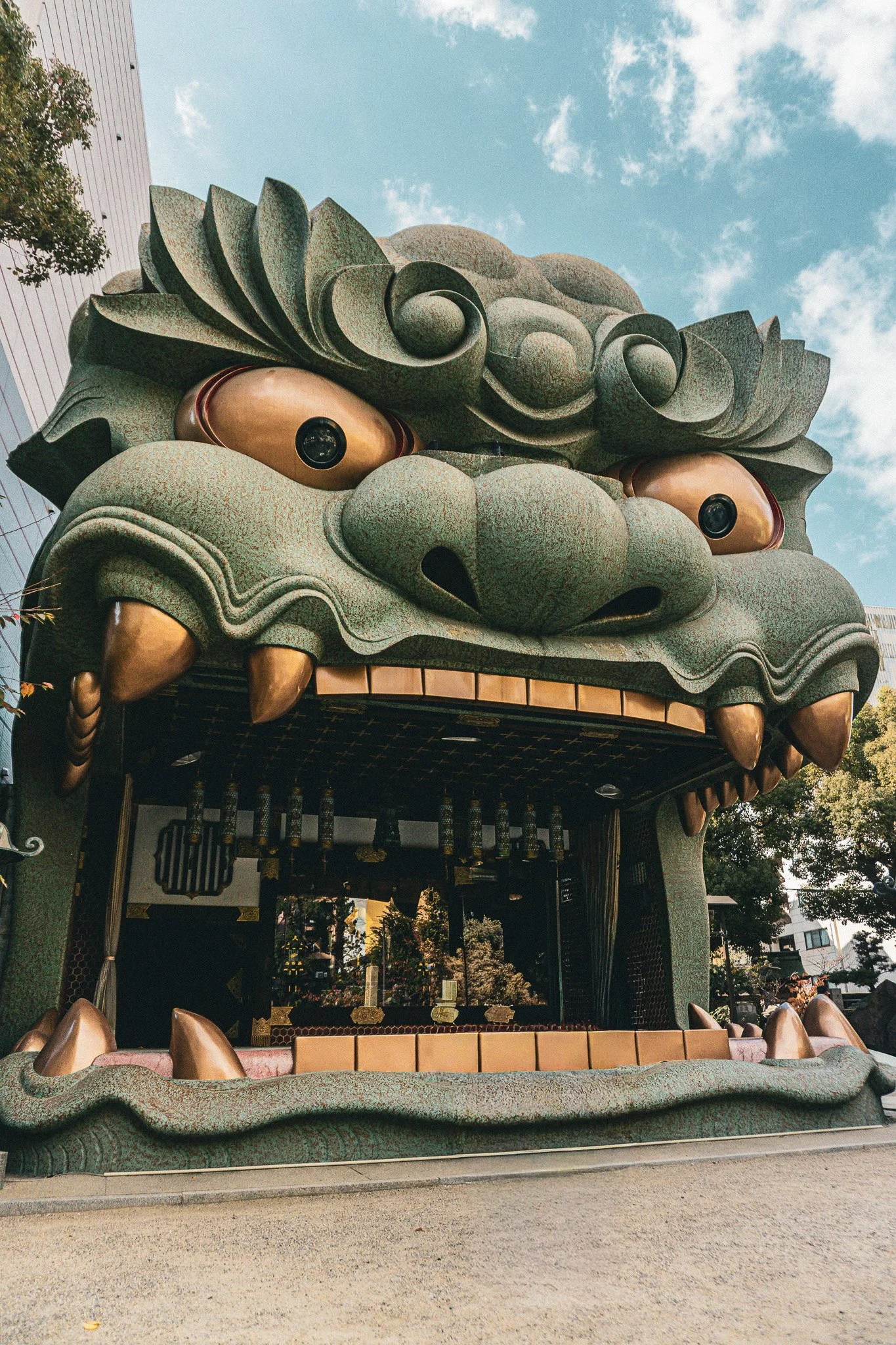 Large decorative Asian-inspired structure resembling a dragon or lion's head with detailed scales, large eyes, and sharp teeth, part of an amusement park or themed attraction.