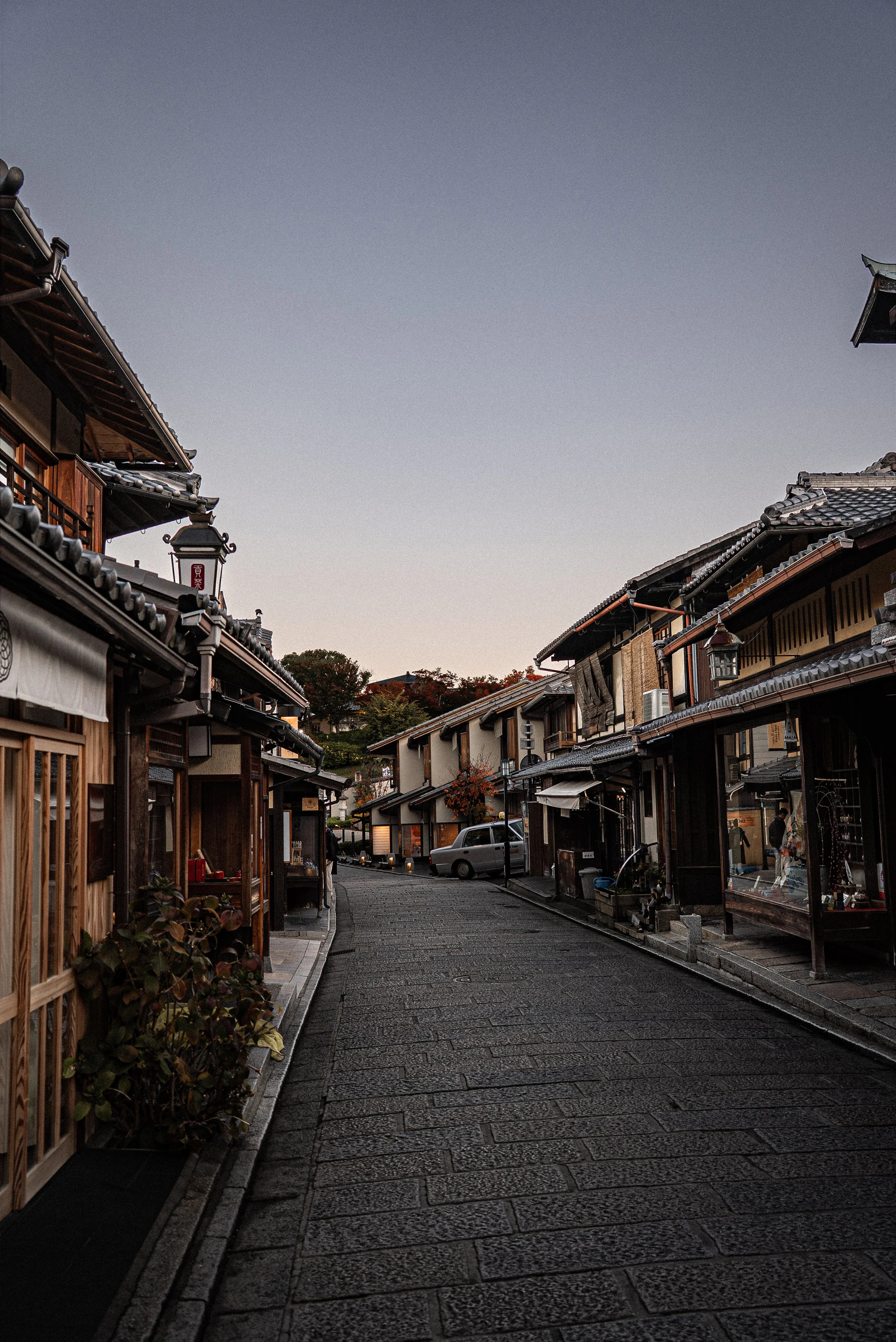 A quiet cobblestone street lined with traditional Japanese wooden buildings with tiled roofs during dusk.
