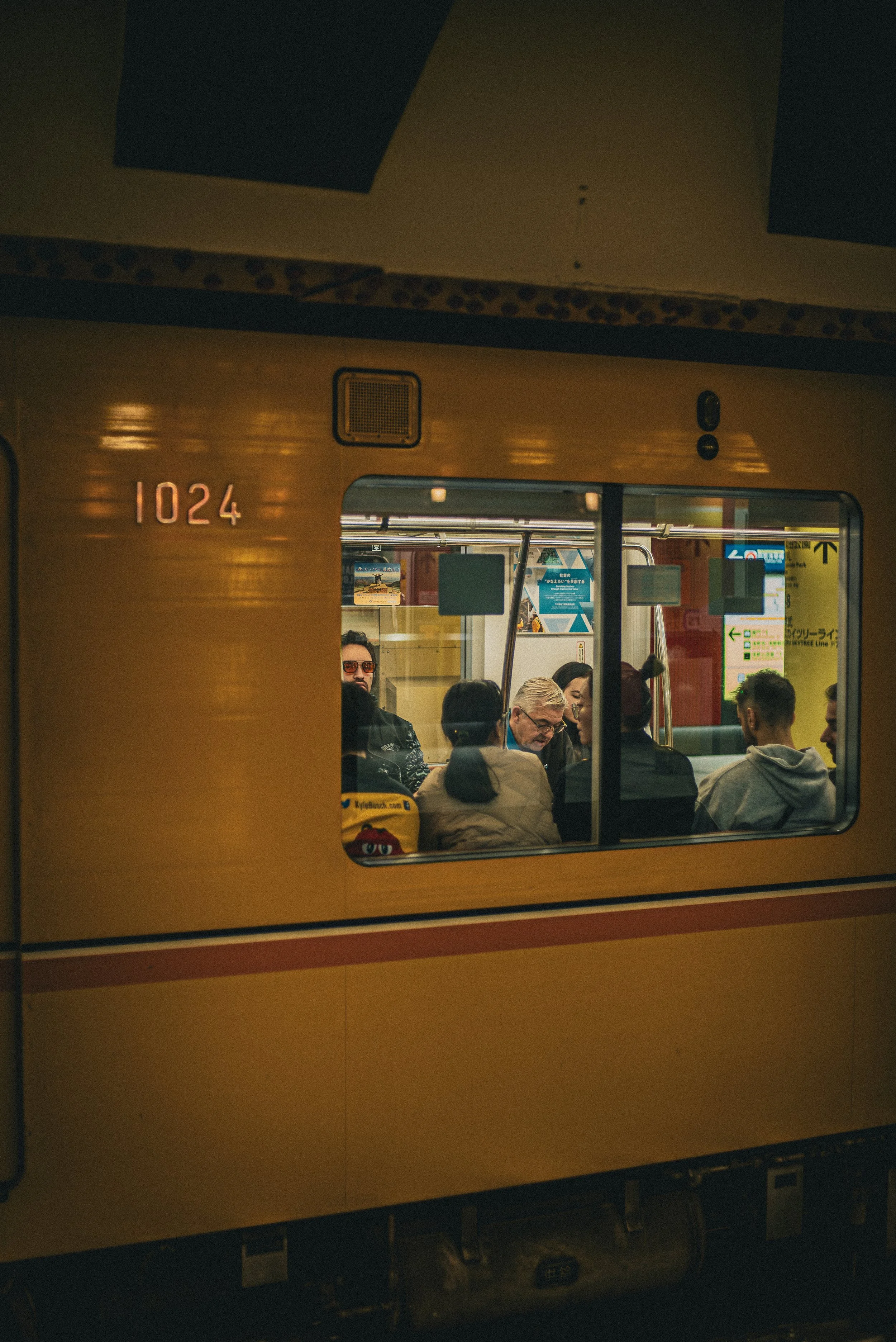 People sitting and talking inside a train, seen through a window with the train number 1024.