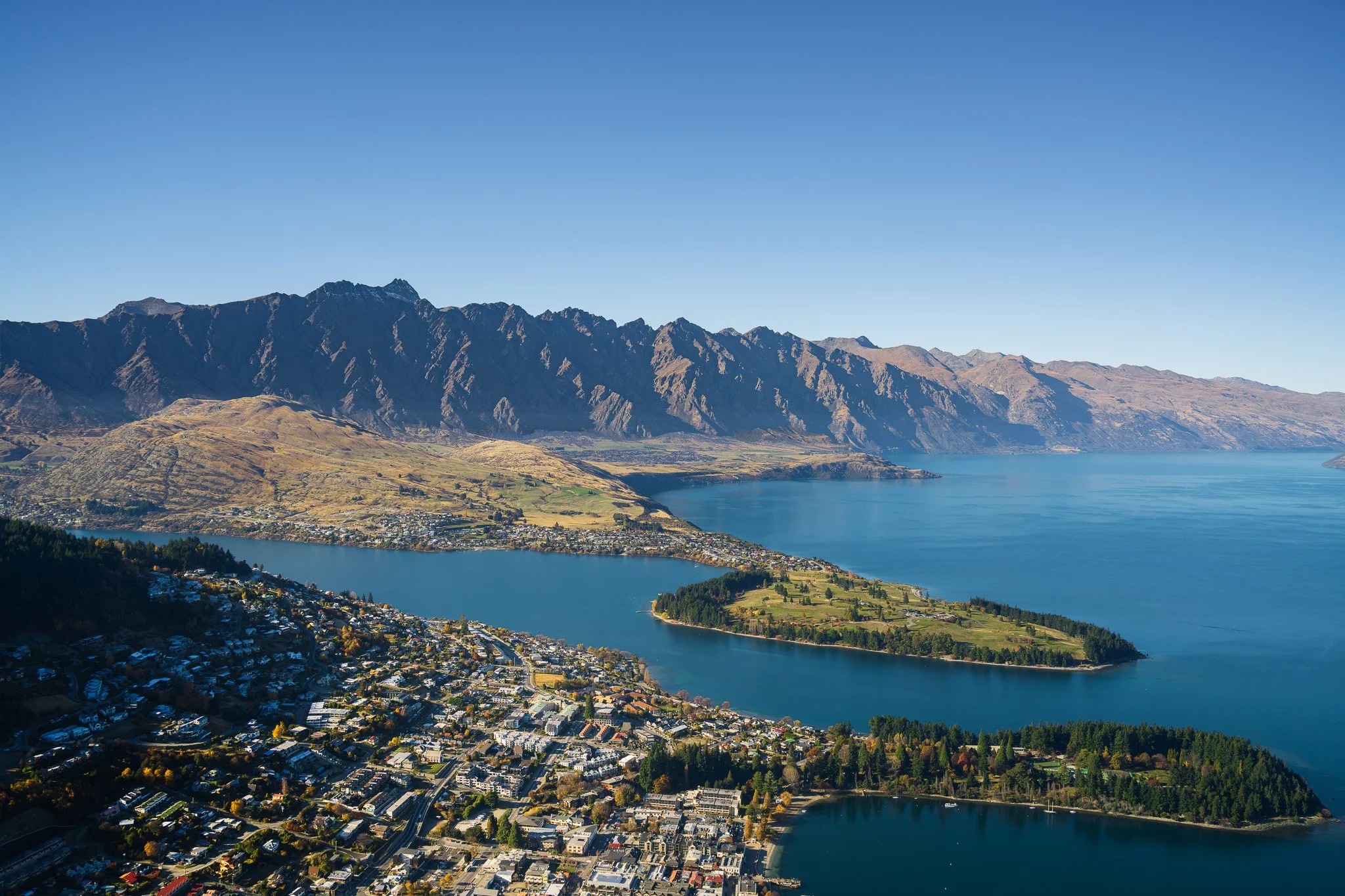 Scenic view of a town alongside a large body of water, with mountains in the background under a clear blue sky.