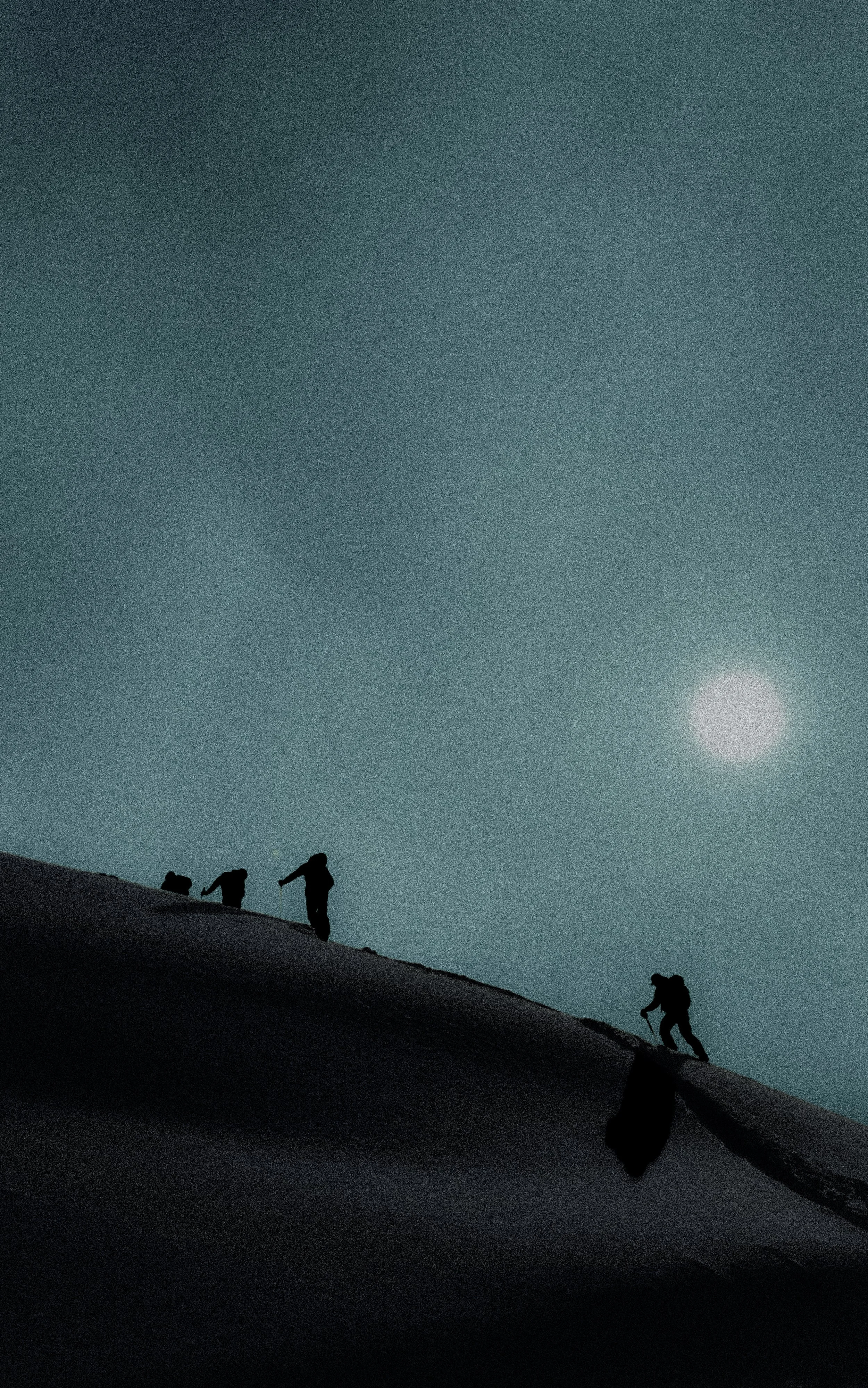 Silhouettes of people hiking on a snowy hill under a cloudy night sky with a bright moon.