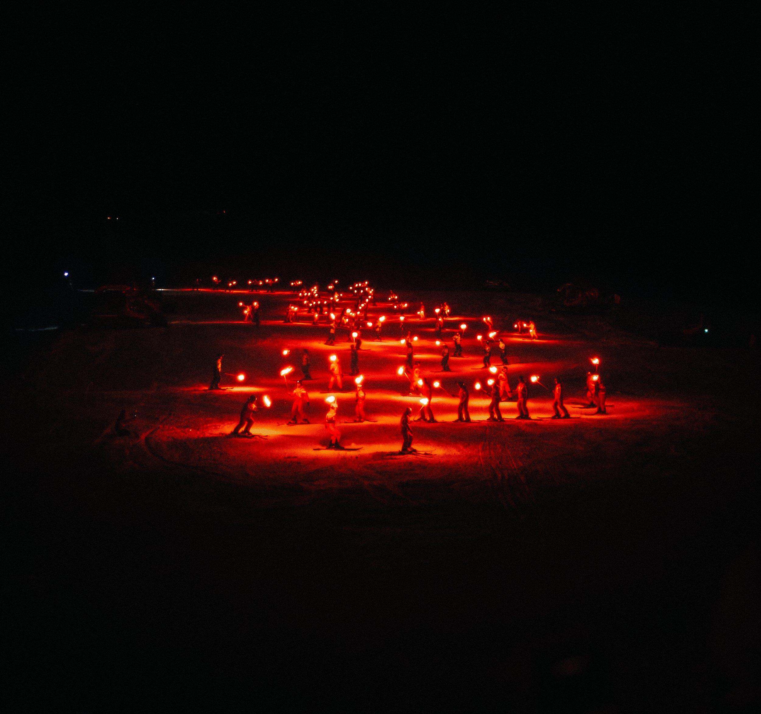 Nighttime scene with red lights and people walking along a path or road.
