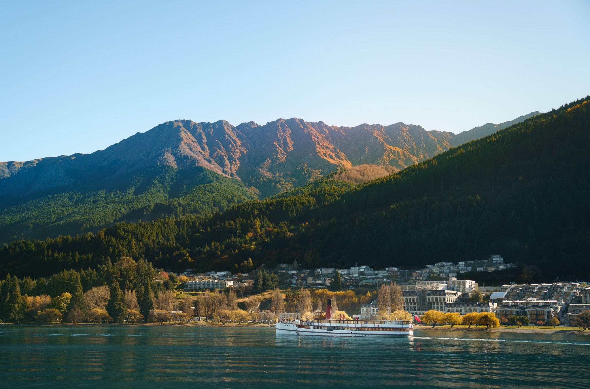 Scenic view of coastal mountains with a small town at the base and a river with a boat in the foreground.
