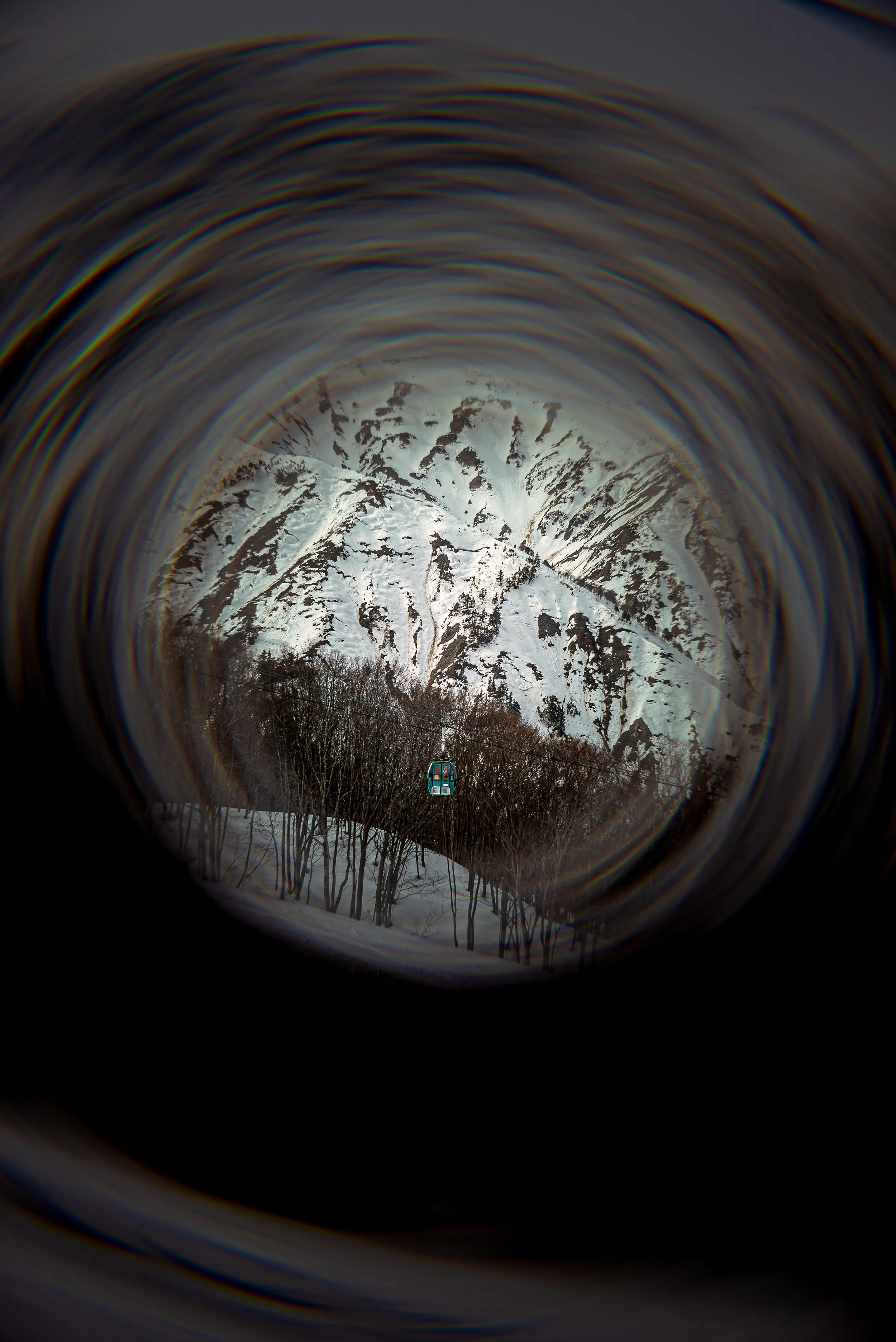 Snow-covered mountain peaks viewed through a circular lens with a cable car in the foreground.