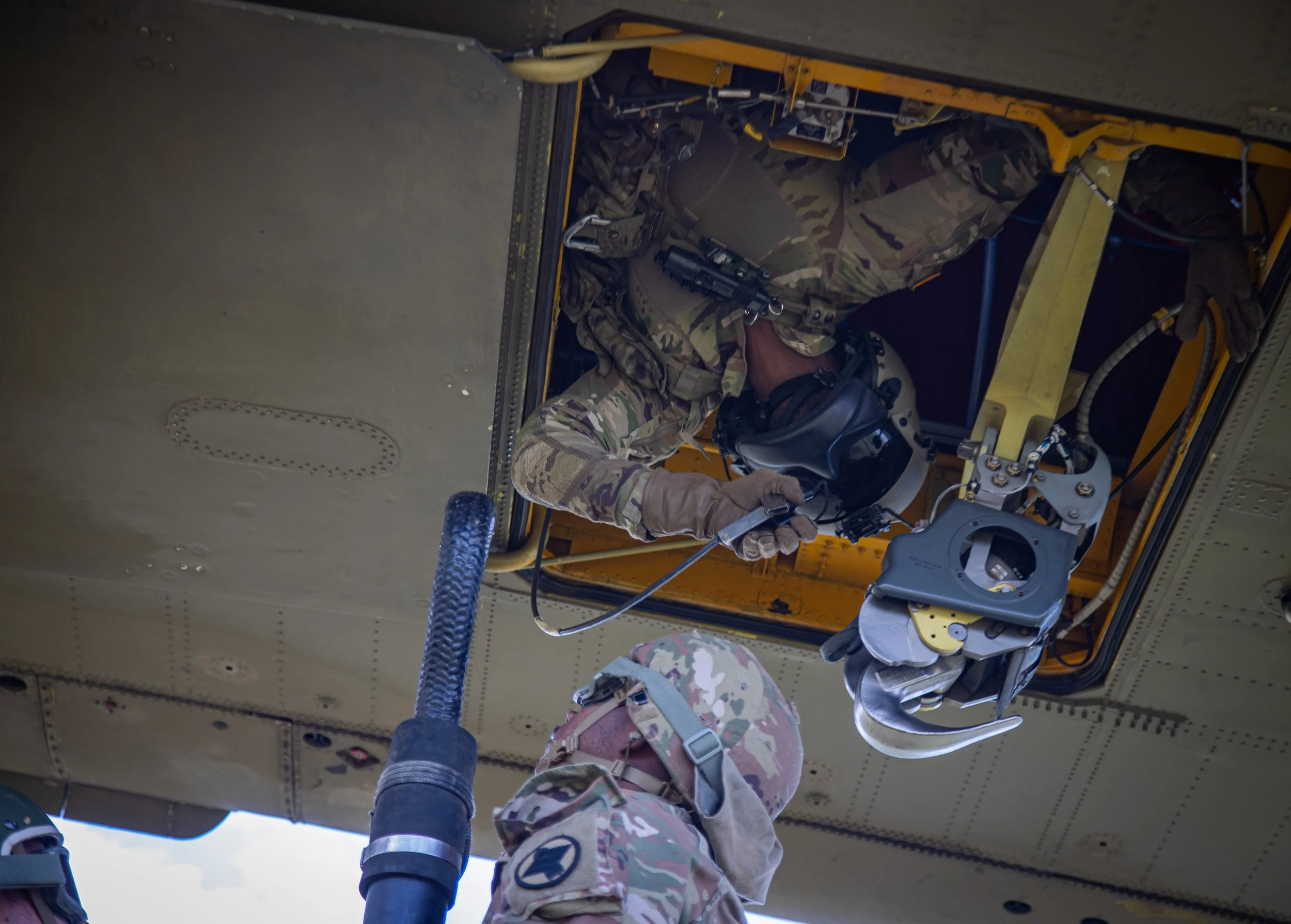 Military personnel working on aircraft, wearing camouflage uniforms and helmets, inside the aircraft's fuselage.