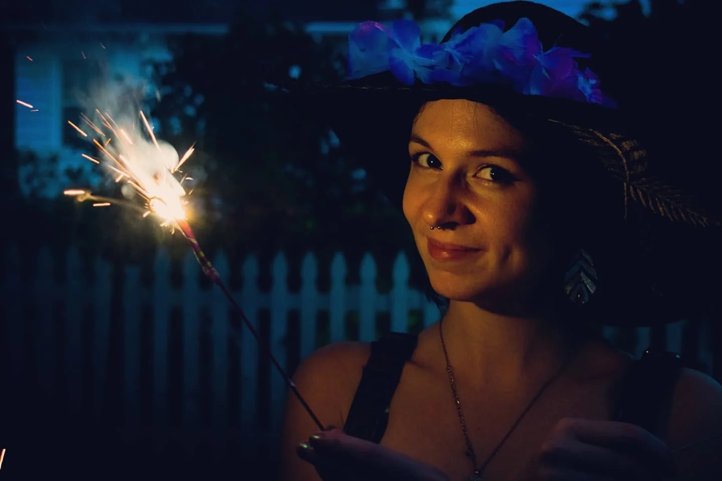Young woman in a witch hat holding a lit sparkler during nighttime celebration.