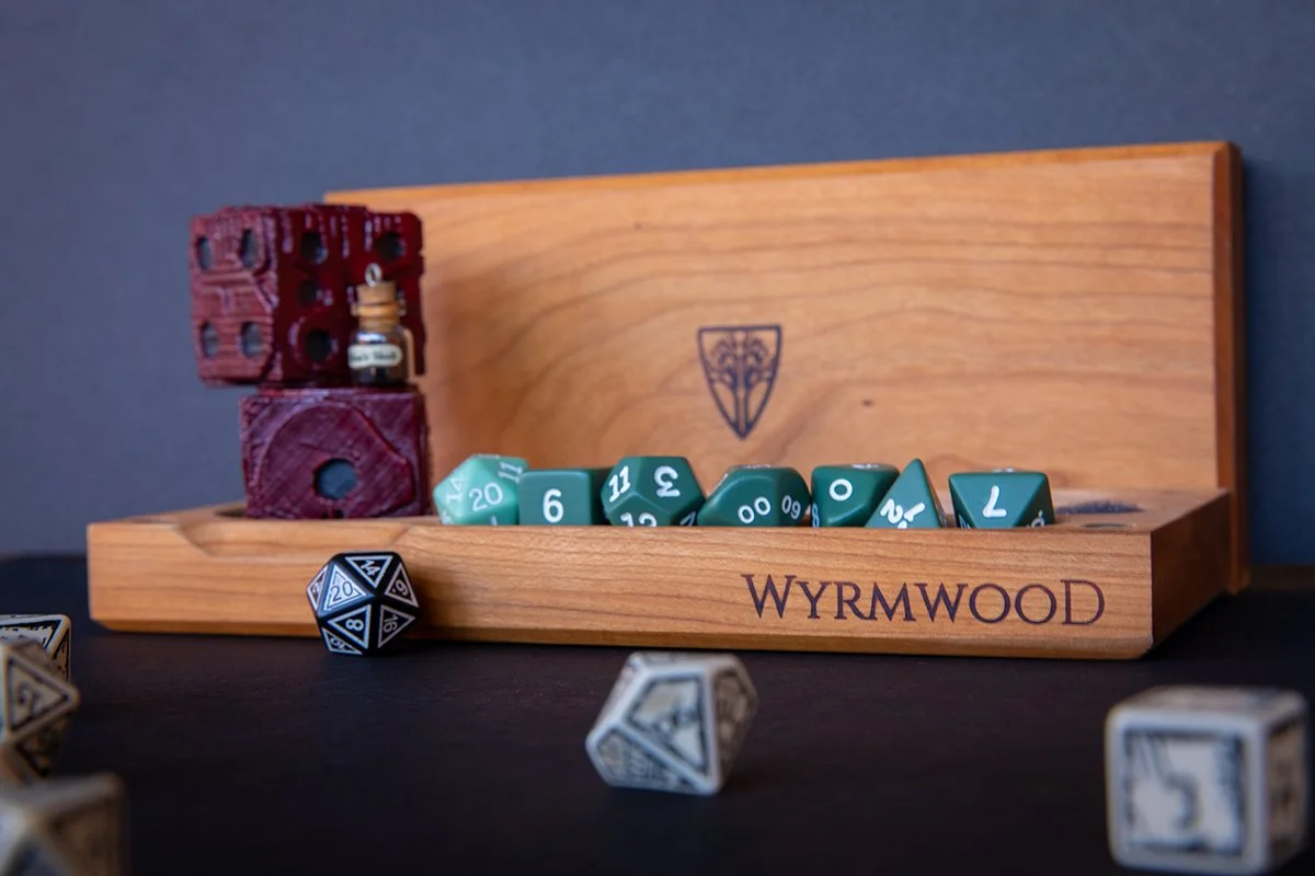 Wooden dice tray with various colorful dice inside and outside, including a black and white 20-sided die and a white die with black numbers, on a dark surface with a blue wall background.