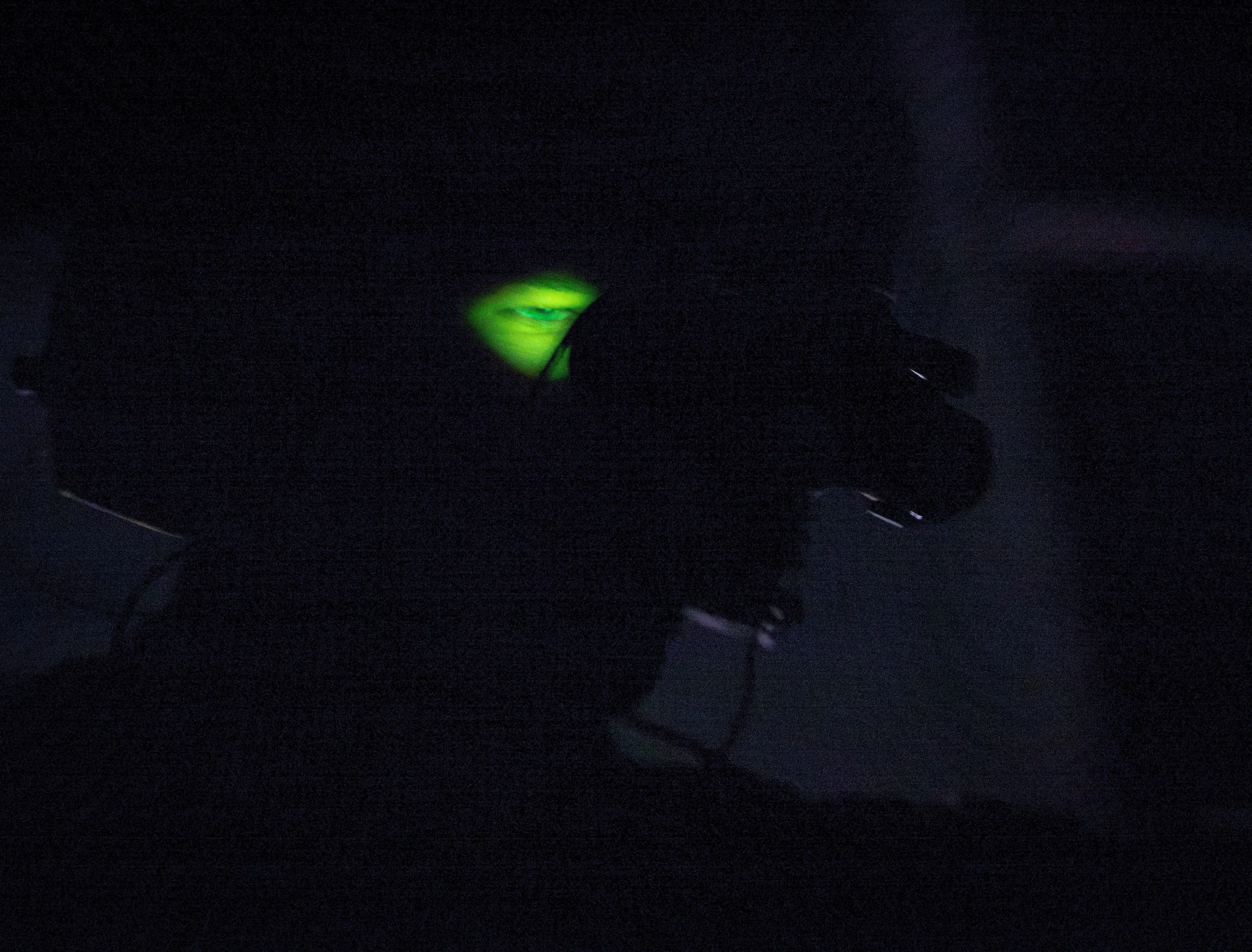 Dark image with a faint green glow and a smiling mouth in the center, surrounded by darkness.