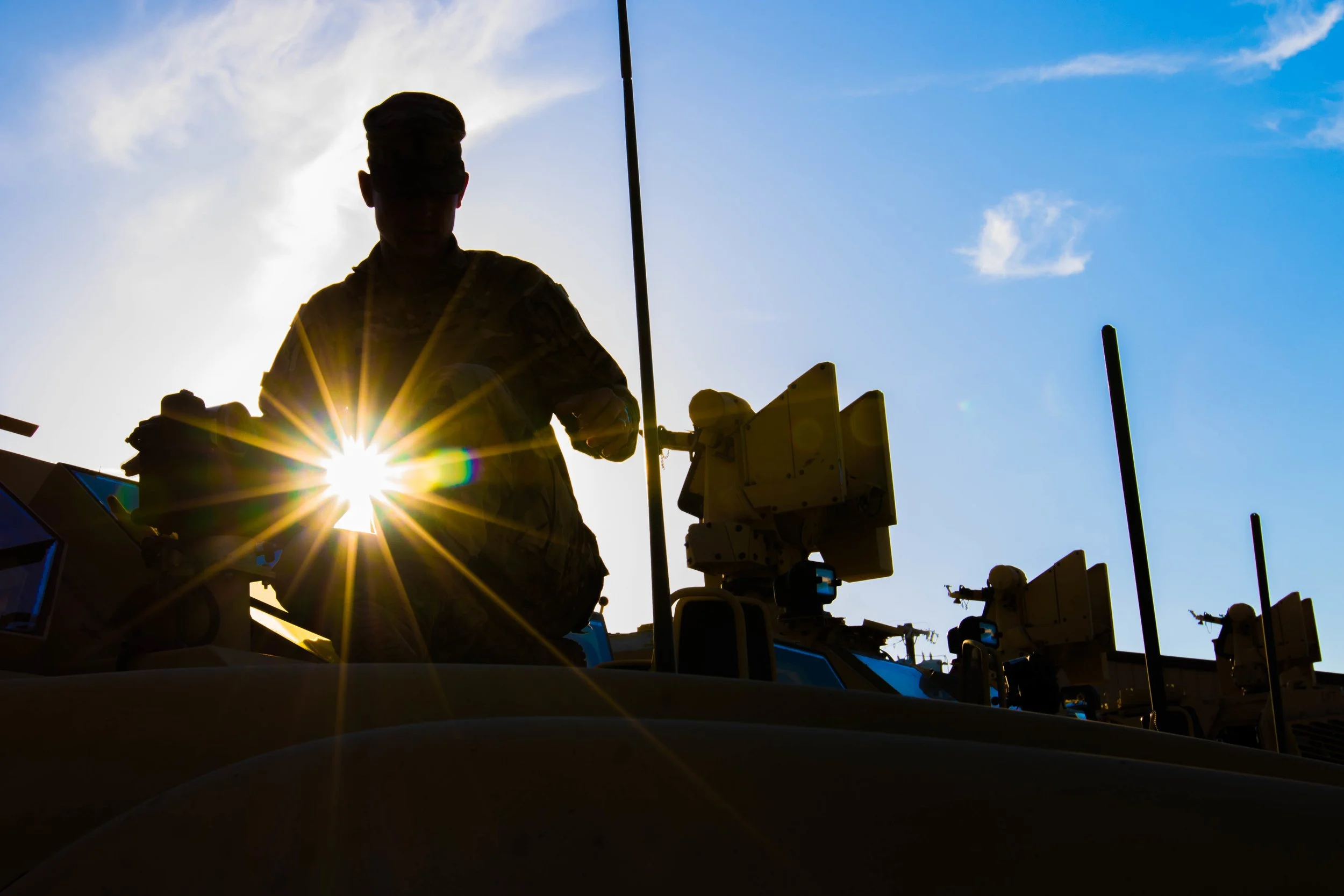 Silhouette of a person working on a rooftop with satellite equipment, backlit by the sun, under a blue sky with some clouds.