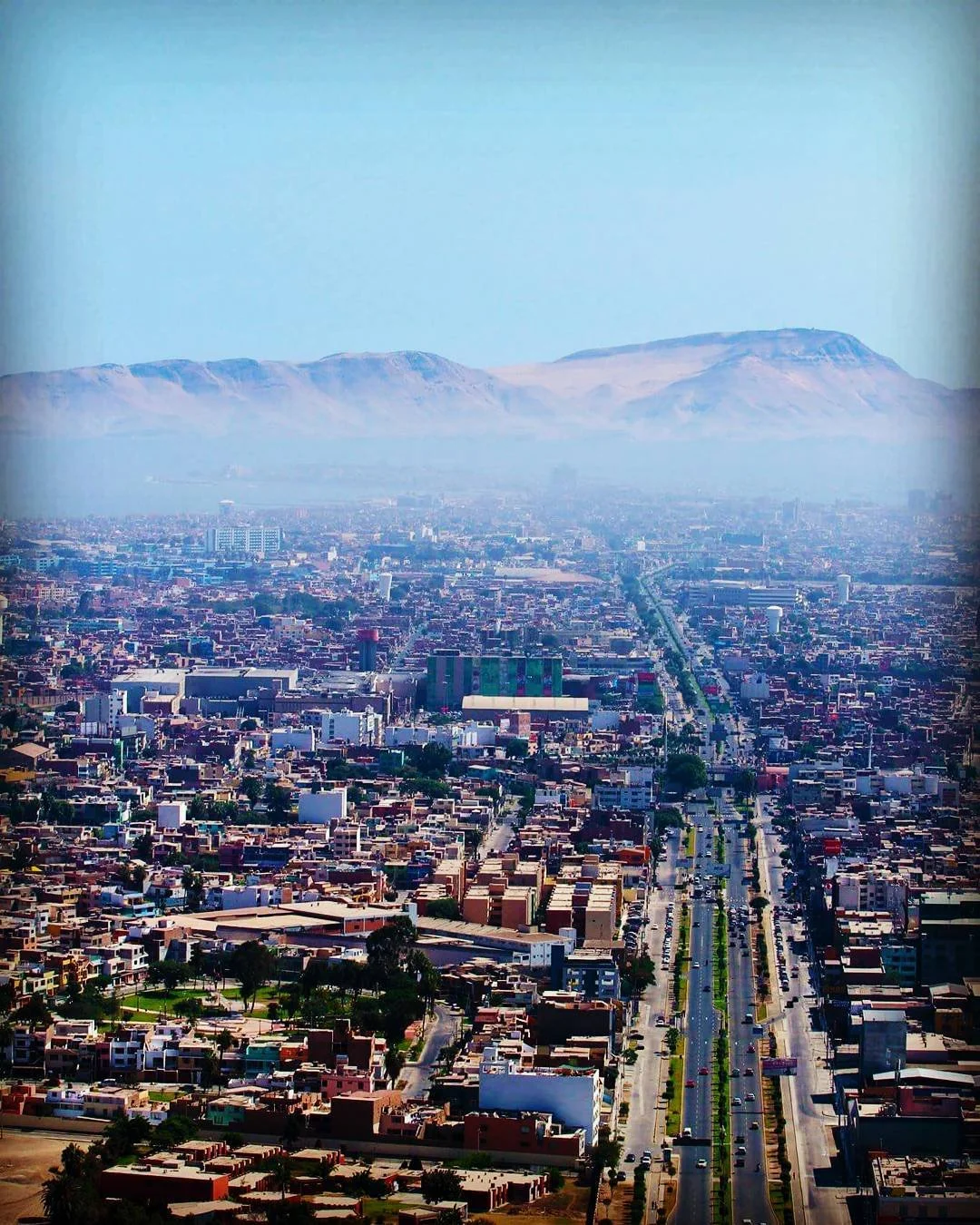 Aerial view of a city with a mountain range in the background, showing streets, buildings, and urban infrastructure.