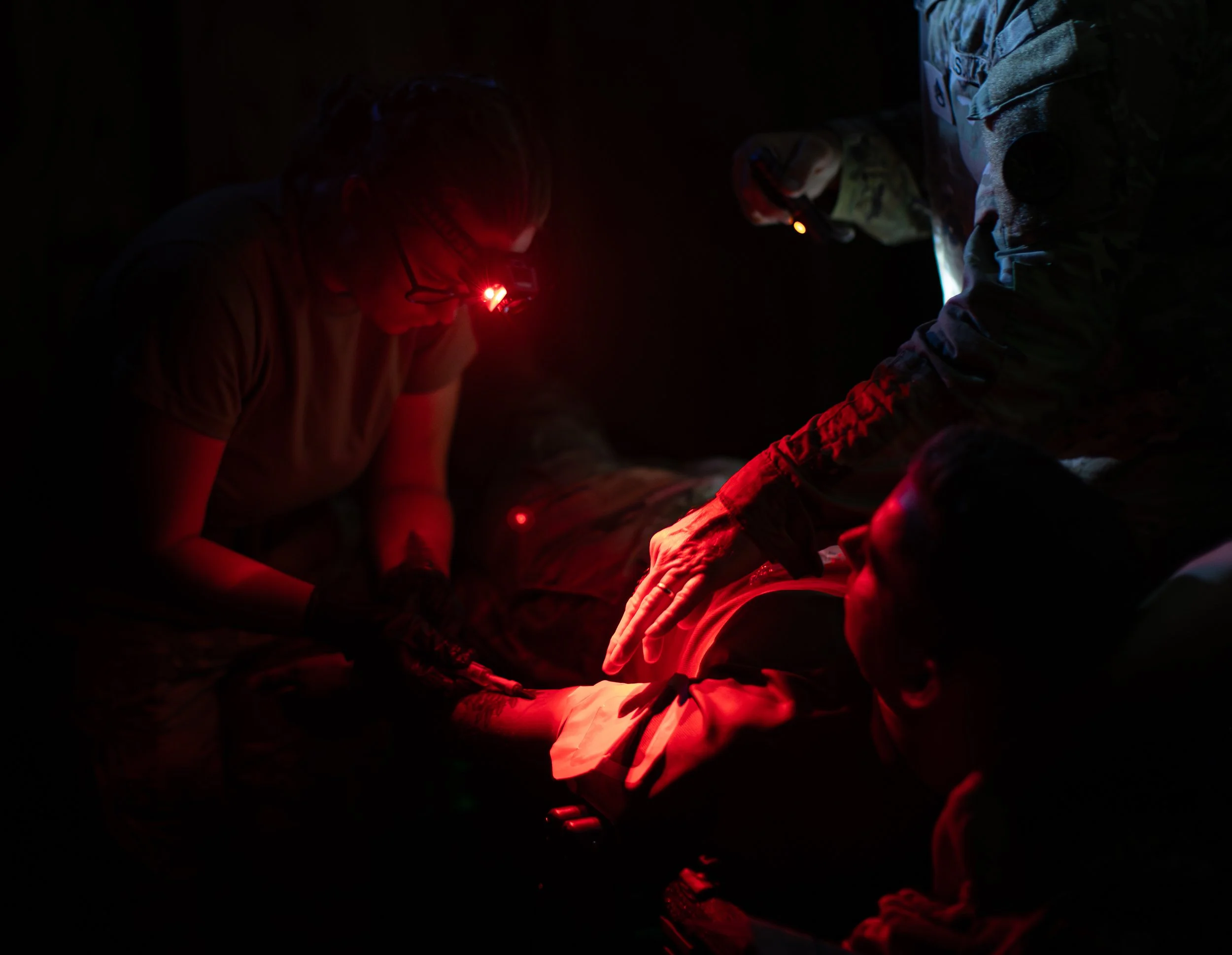People wearing headlamps sitting on the ground in a dark environment, illuminated by red lights, possibly indicating a nighttime activity or rescue operation.