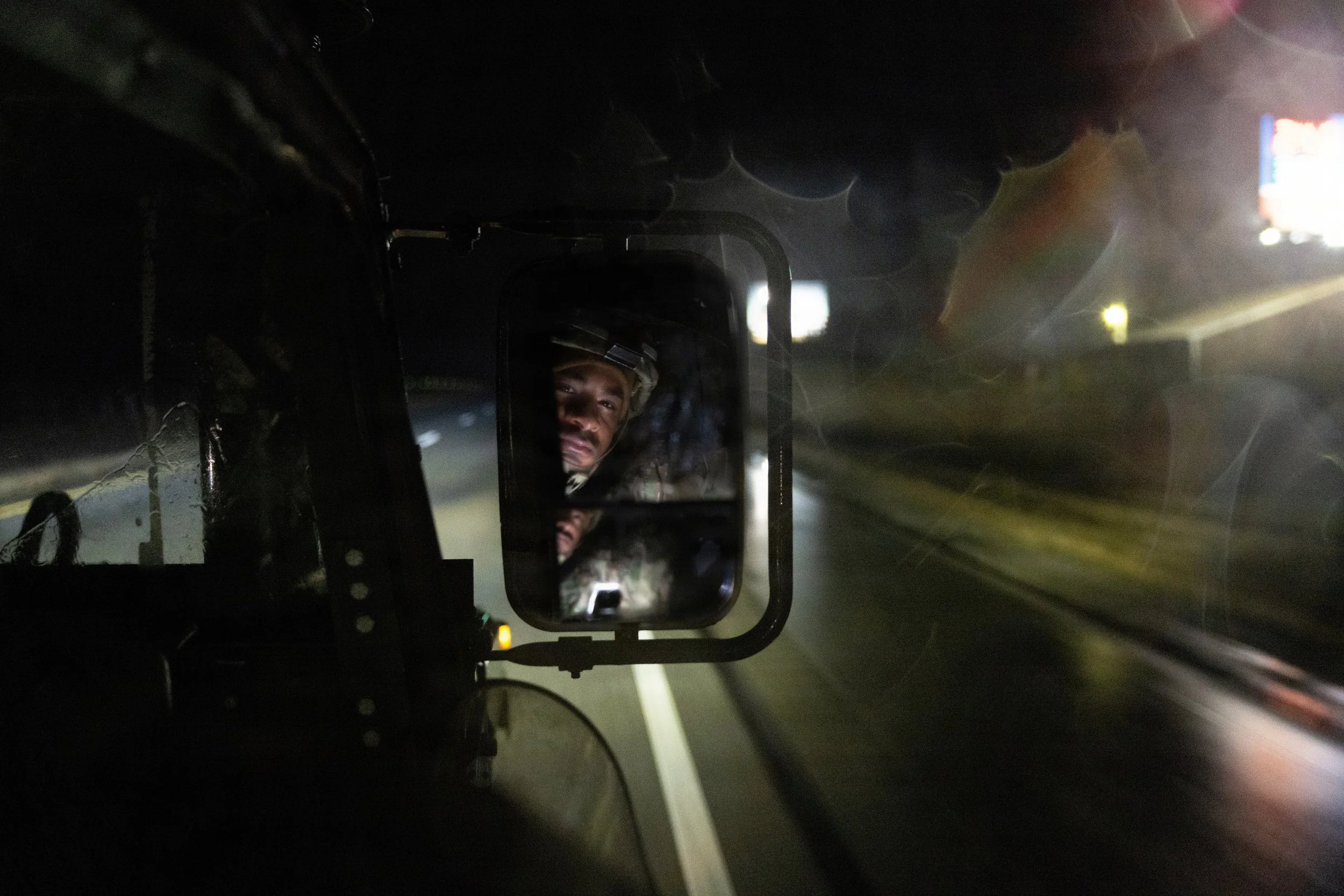 Driver taking a selfie on a mobile phone while driving at night, with a reflection of their face visible in the rearview mirror.