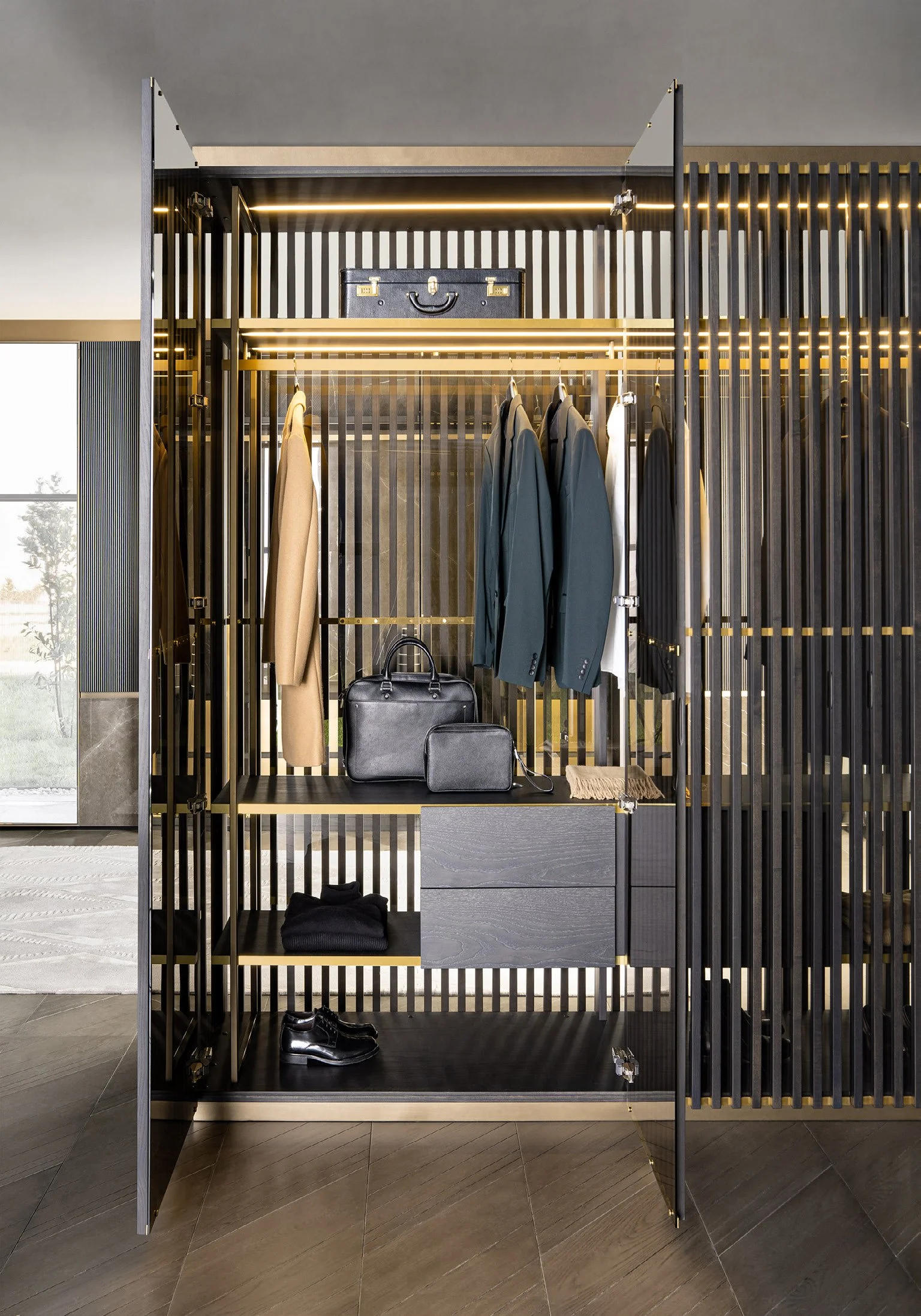 Modern wardrobe with black metal frame and golden accents, containing hanging jackets, a black briefcase, and shoes on the floor.