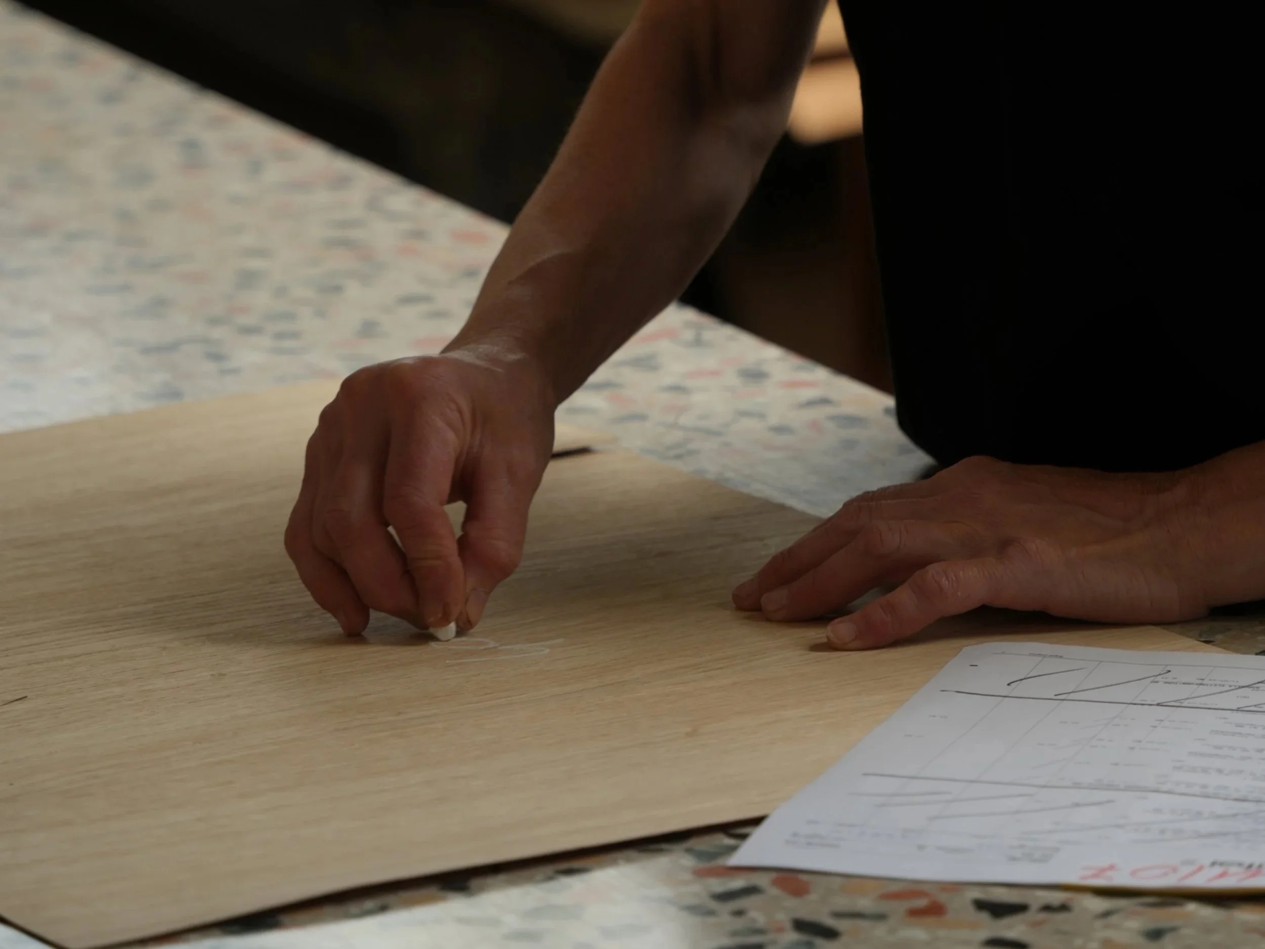 Close-up of two hands on a wooden table making edits on design papers.