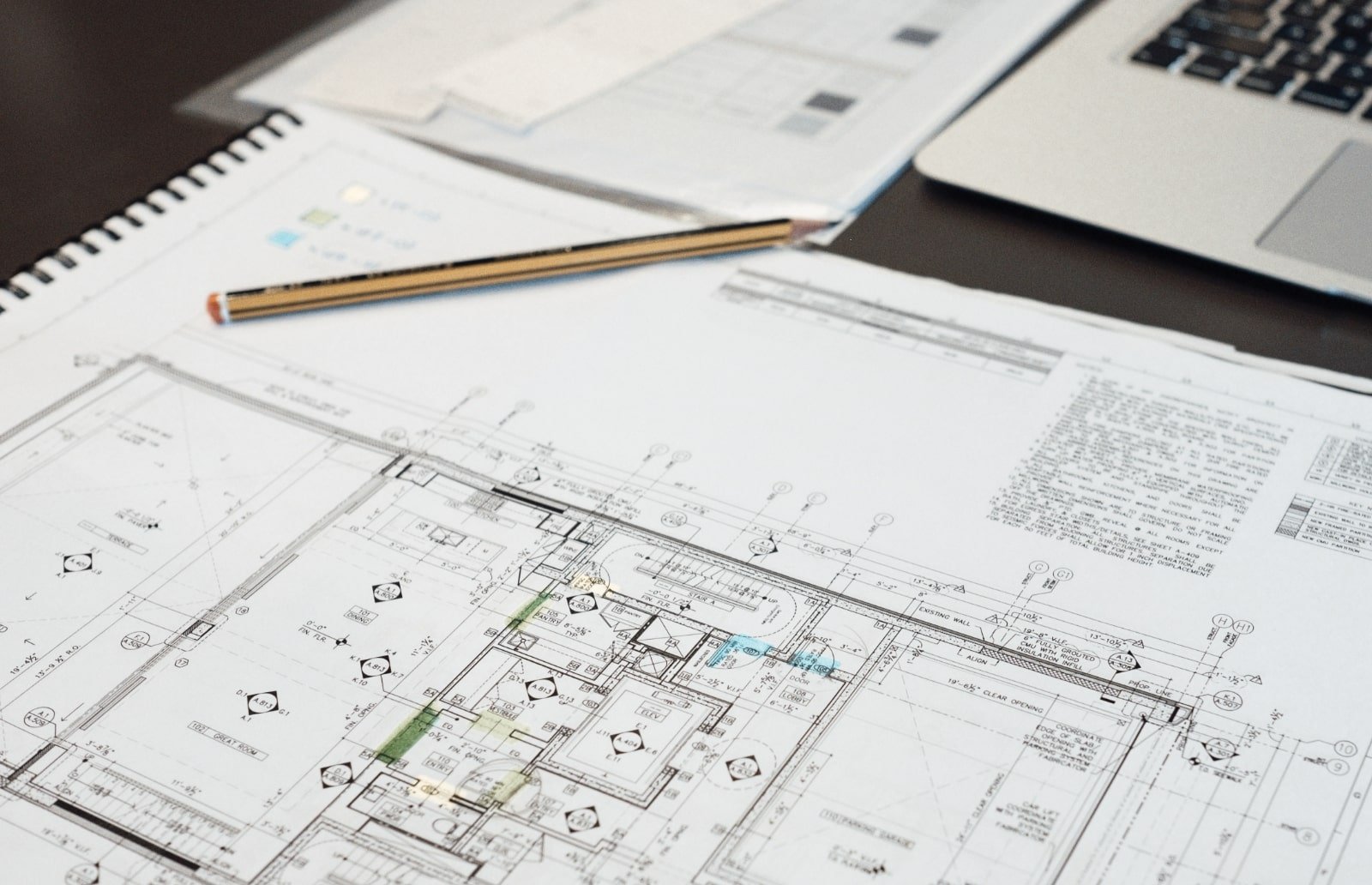 Architectural blueprints and floor plans on a desk with a laptop and a pencil.