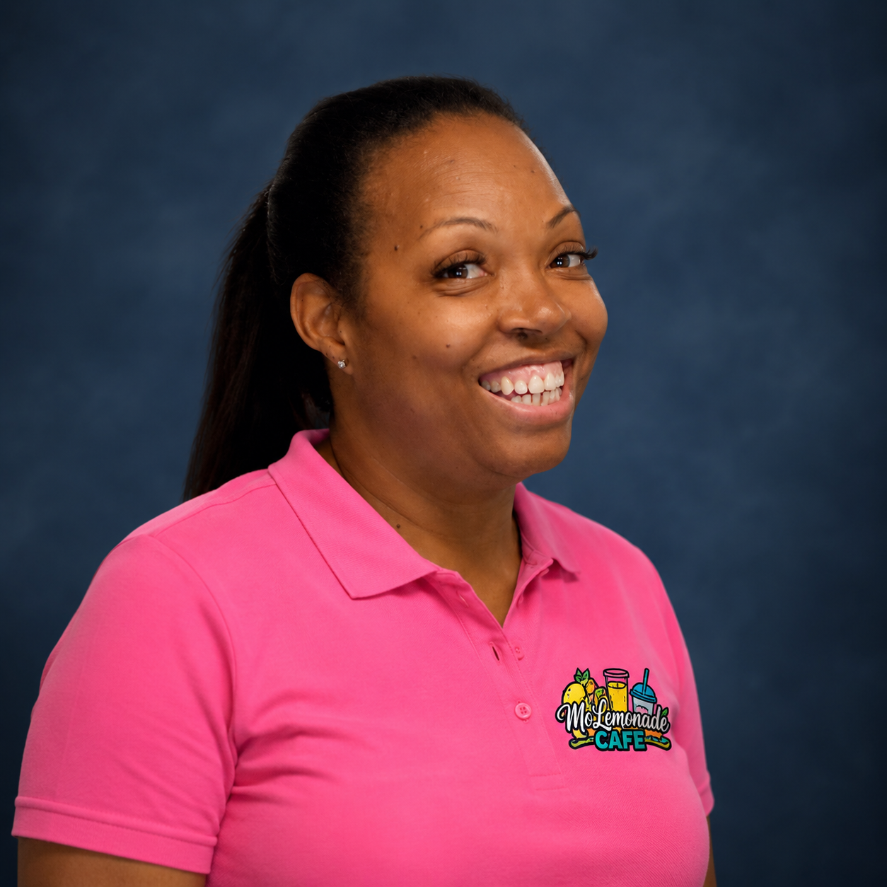 A woman smiling wearing a pink polo shirt with a logo for Mo Lemonade Cafe, standing against a dark blue background.